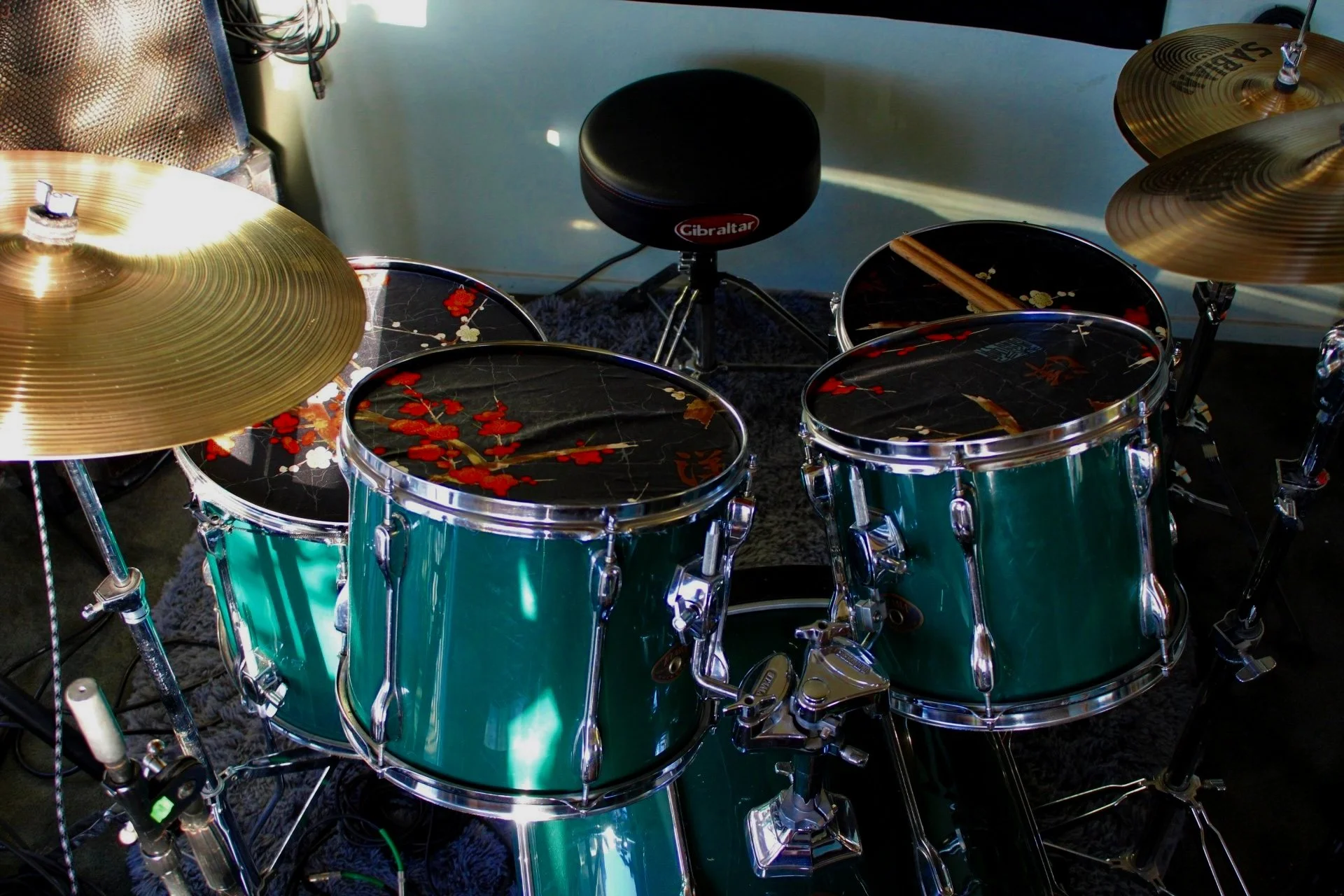 Drum kit with green drums and cymbals, including a stool and drumsticks on top of a drum.