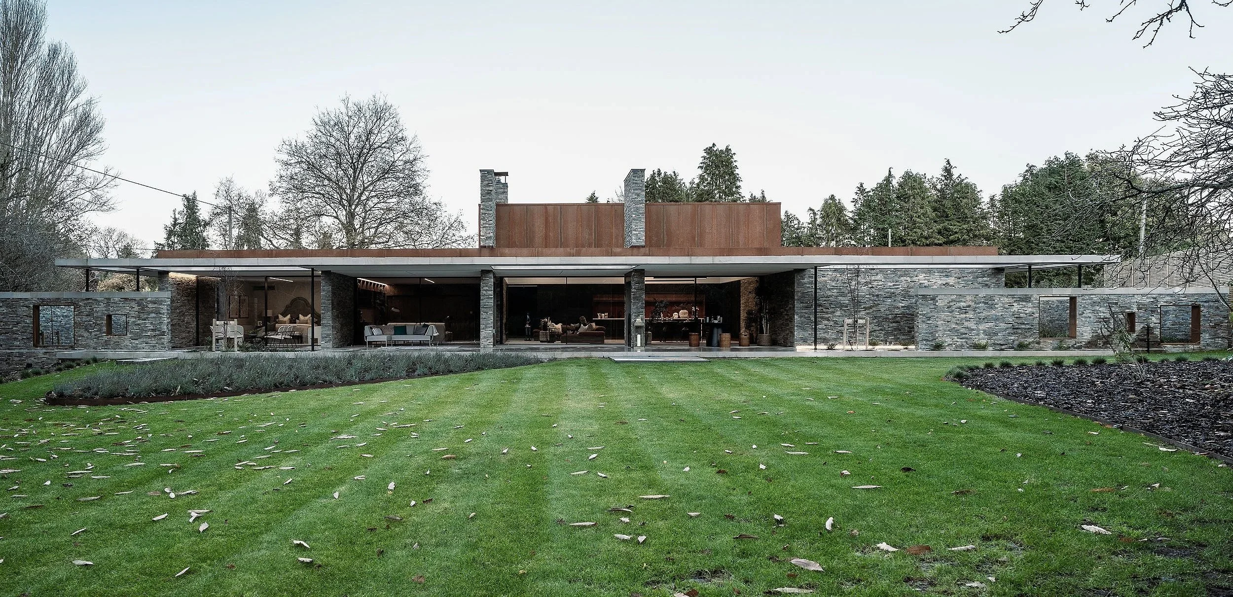 Modern house with stone walls, large glass windows, and a spacious green front yard.