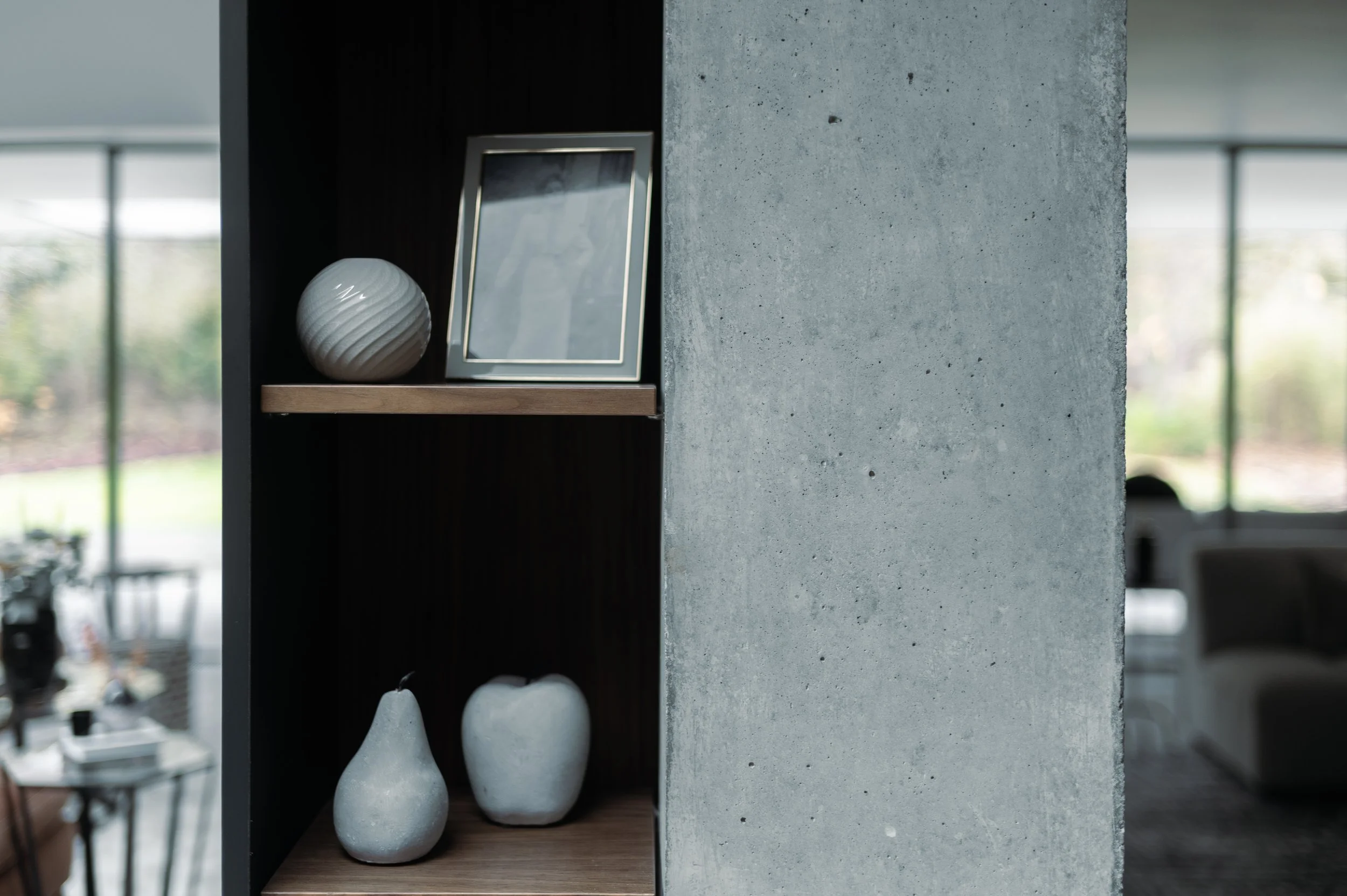 Decorative objects on a wooden shelf inside a modern home, including a white textured spherical vase, a framed picture, and three white vases with varying heights.