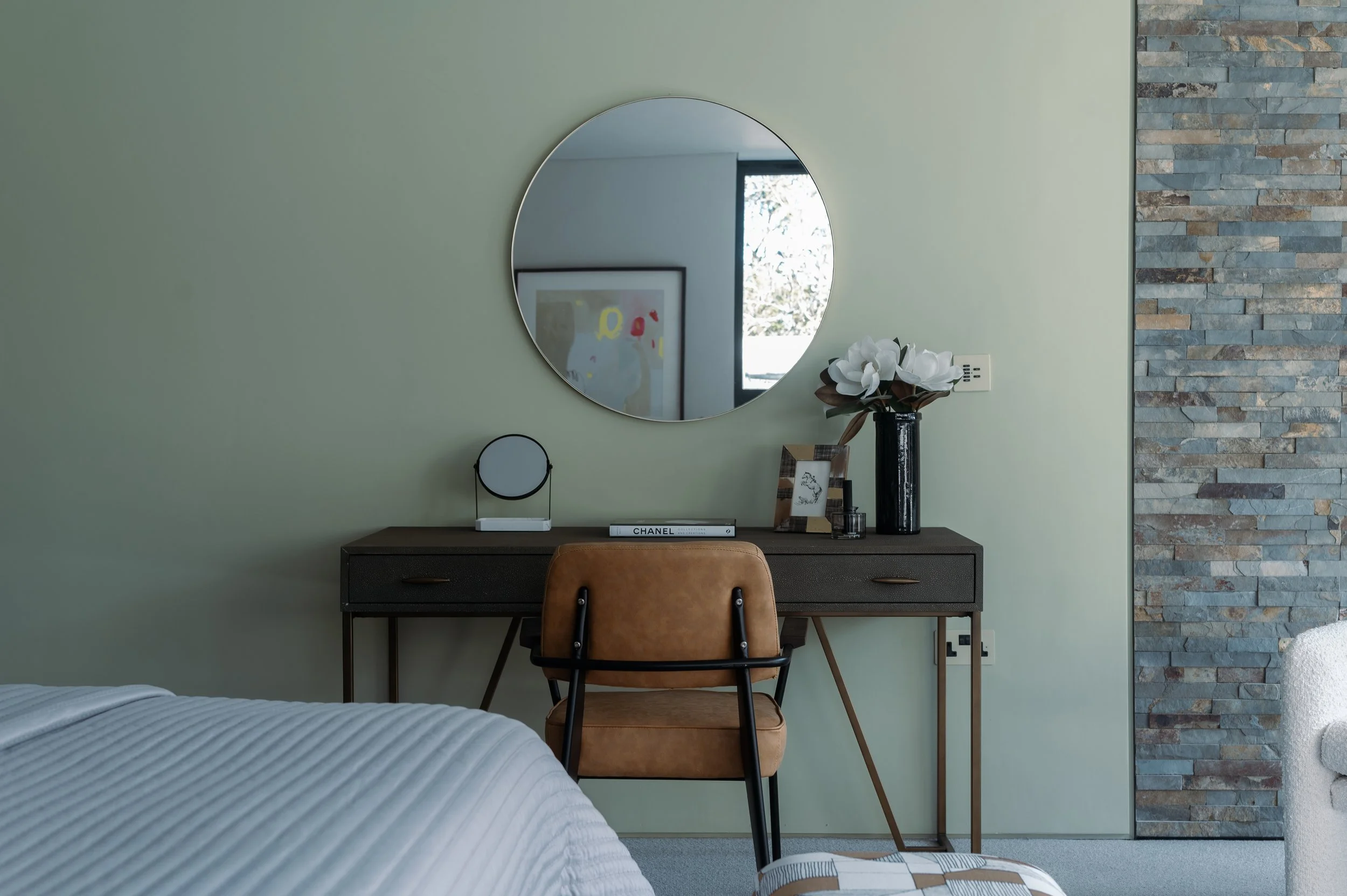 Bedroom with a desk, mirror, and decorative items against a green wall, with a stone accent wall on the right side.