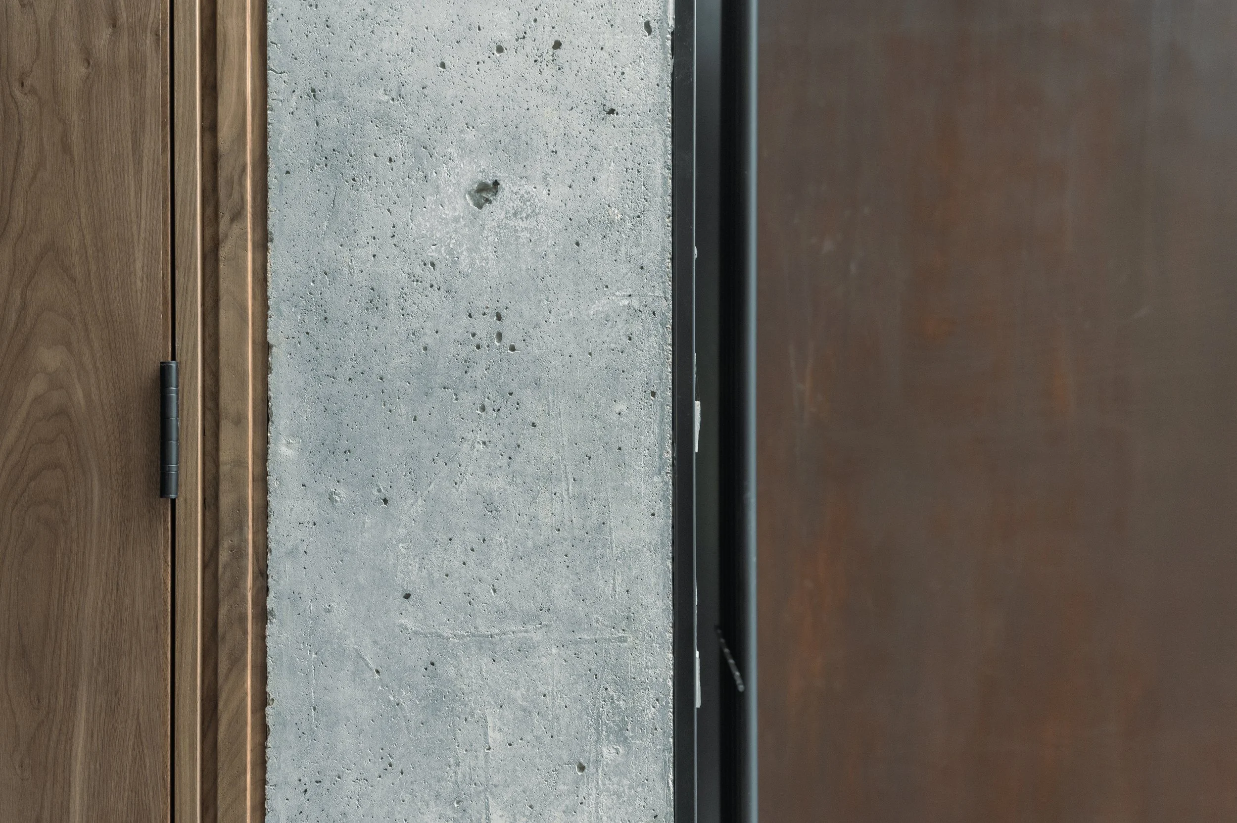Close-up of a modern kitchen countertop with a concrete surface, wooden cabinetry, and a black metal element.