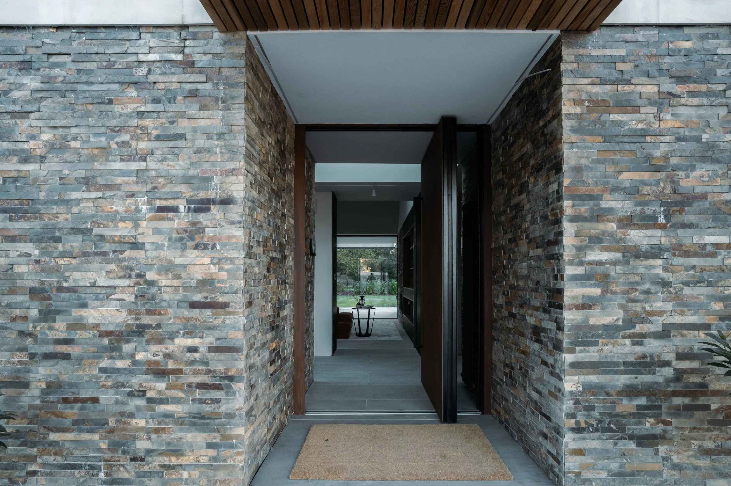Entryway with stone walls, doorway, view of living room, and a doormat.