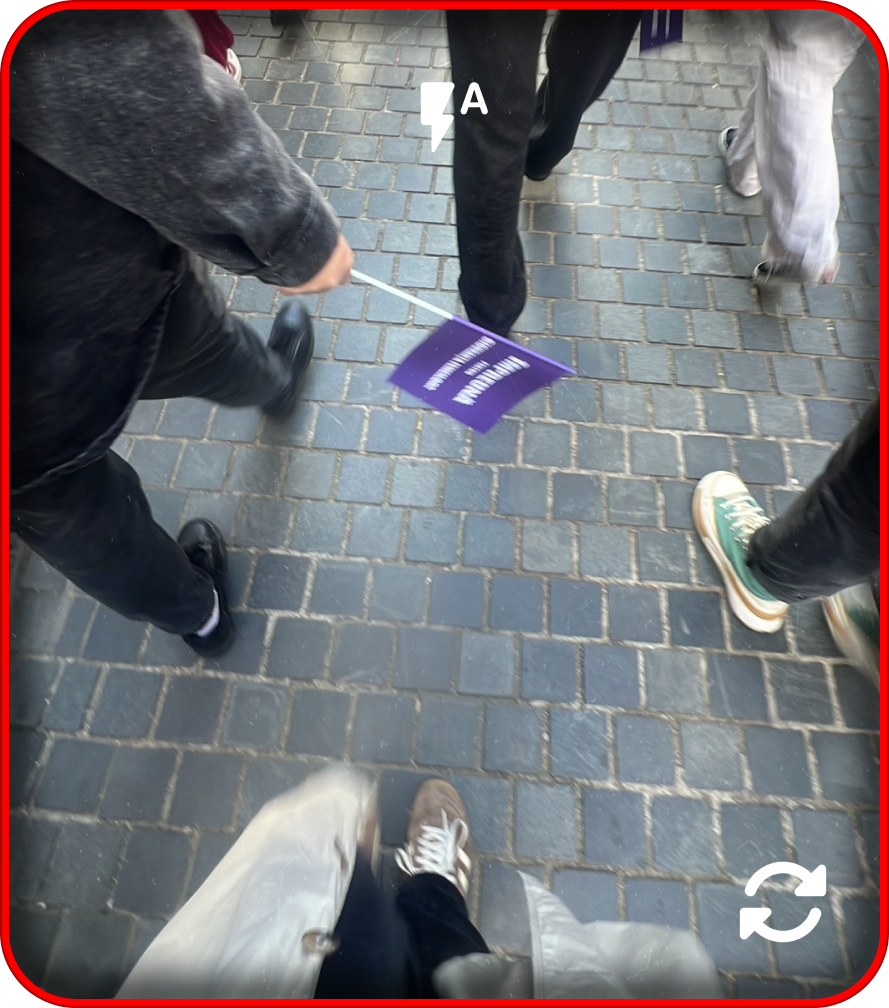 People walking on a cobblestone street, with one person holding a purple flag.