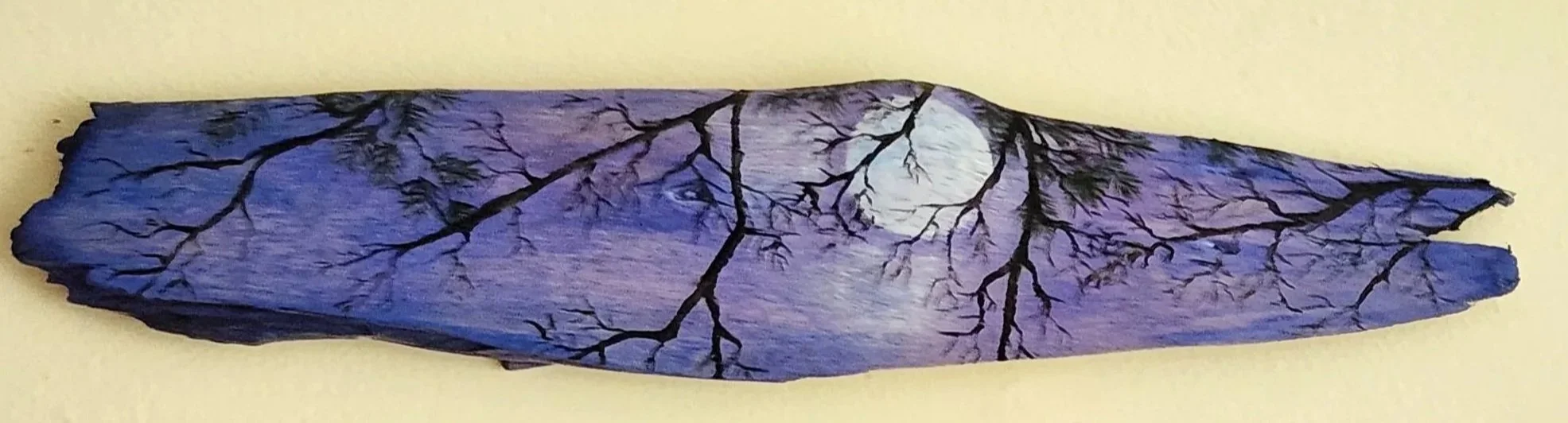 Piece of wood or bark with painted moon and tree branches, set against a light-colored background.