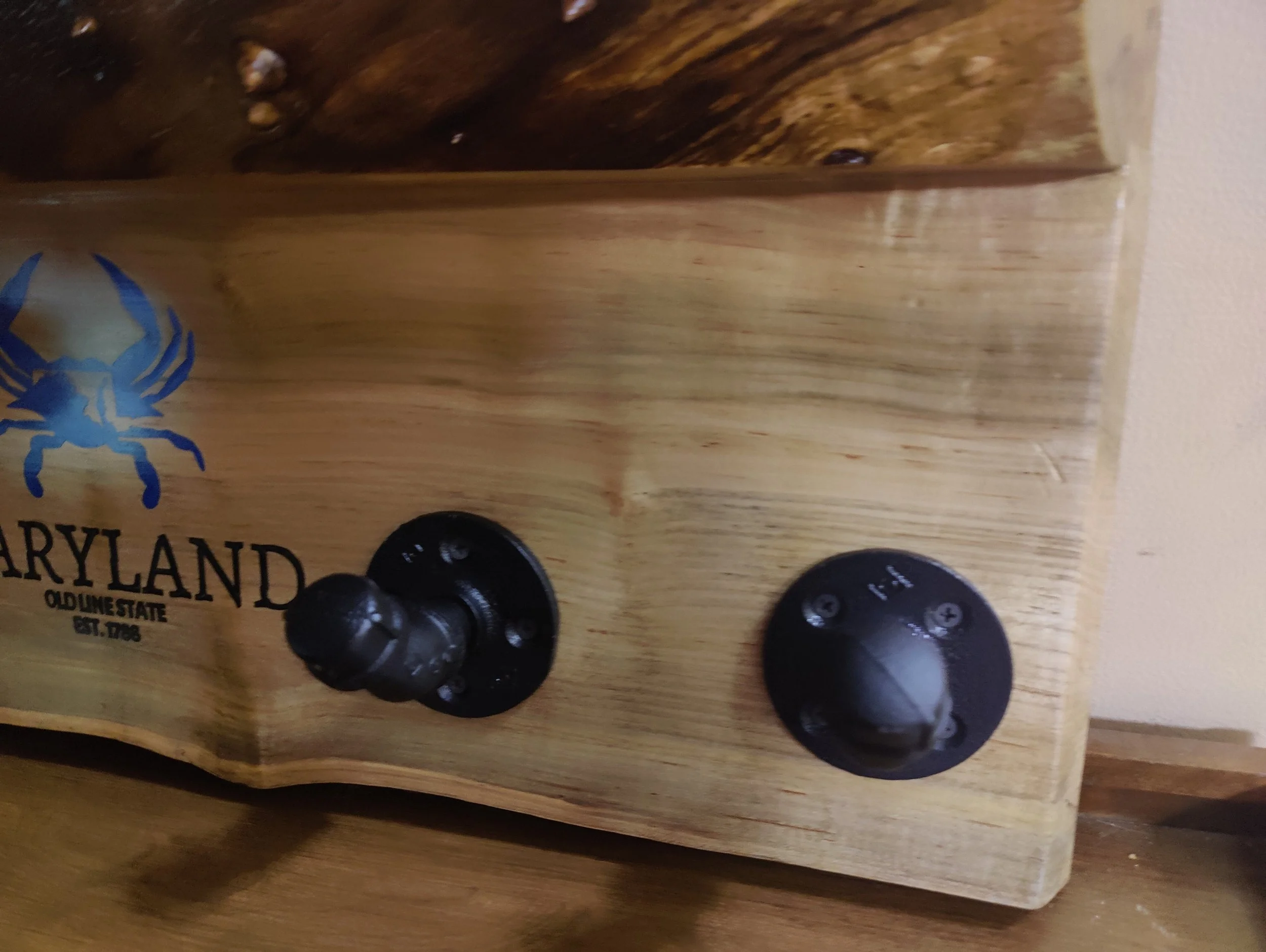 Close-up of a wooden Maryland souvenir box with two black knobs, one with a small handle and a round black label with screws.