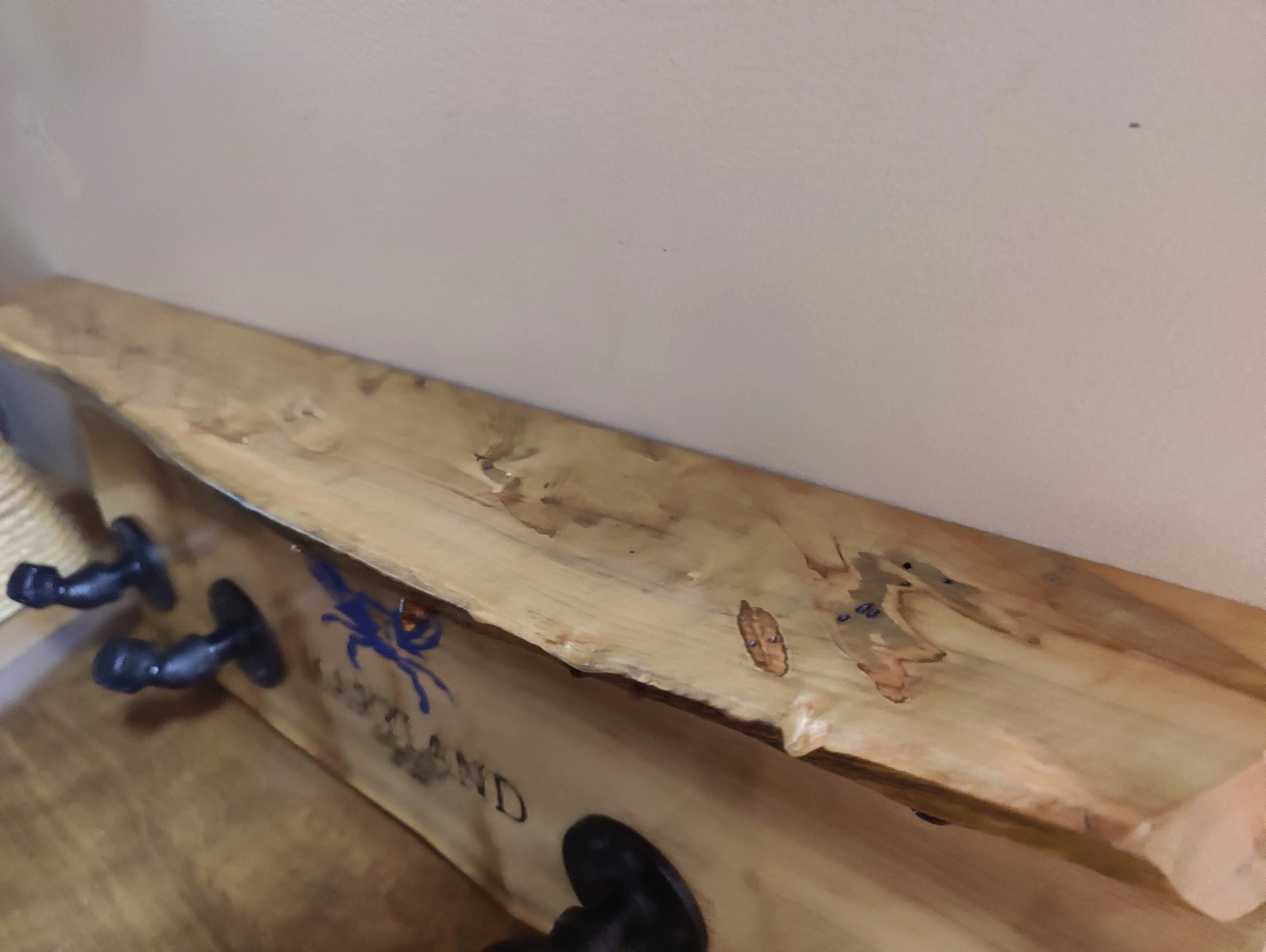 Close-up of a wooden sandbox with a chipped and rough edge, and black plastic toys attached to the side, against a plain wall background.