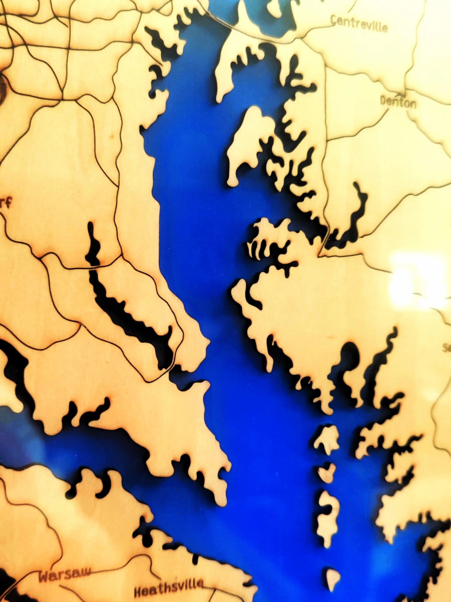 Close-up of a wooden map showing a reservoir with a blue color, detailed with surrounding cities including Warsaw, Heathrow, and Denton.