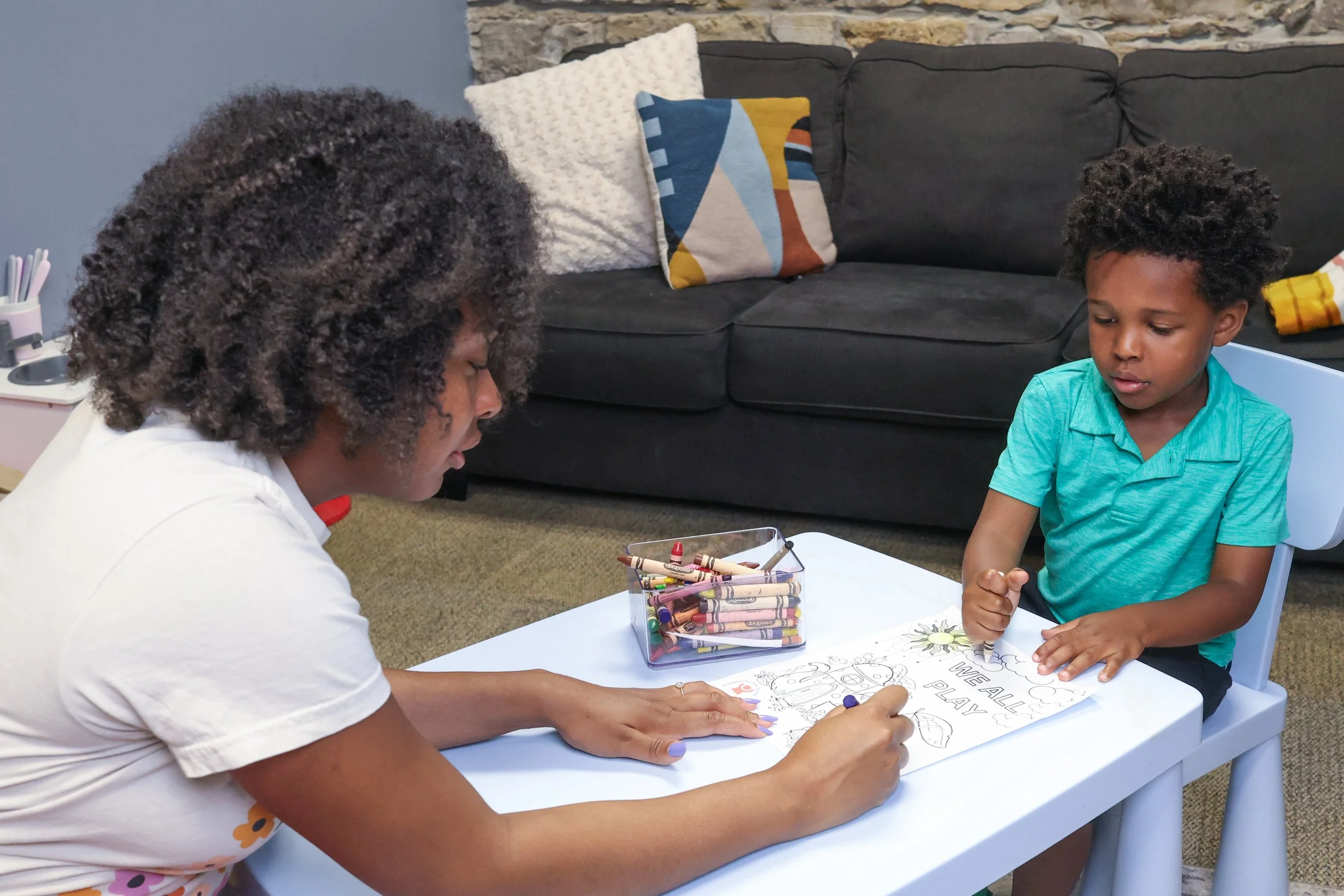 A Black woman therapist sits at a small table and colors with a Black child. Starting play therapy can and should be fun not scary. Let us help you get started with calm and confidence--call us for a free consultation today!