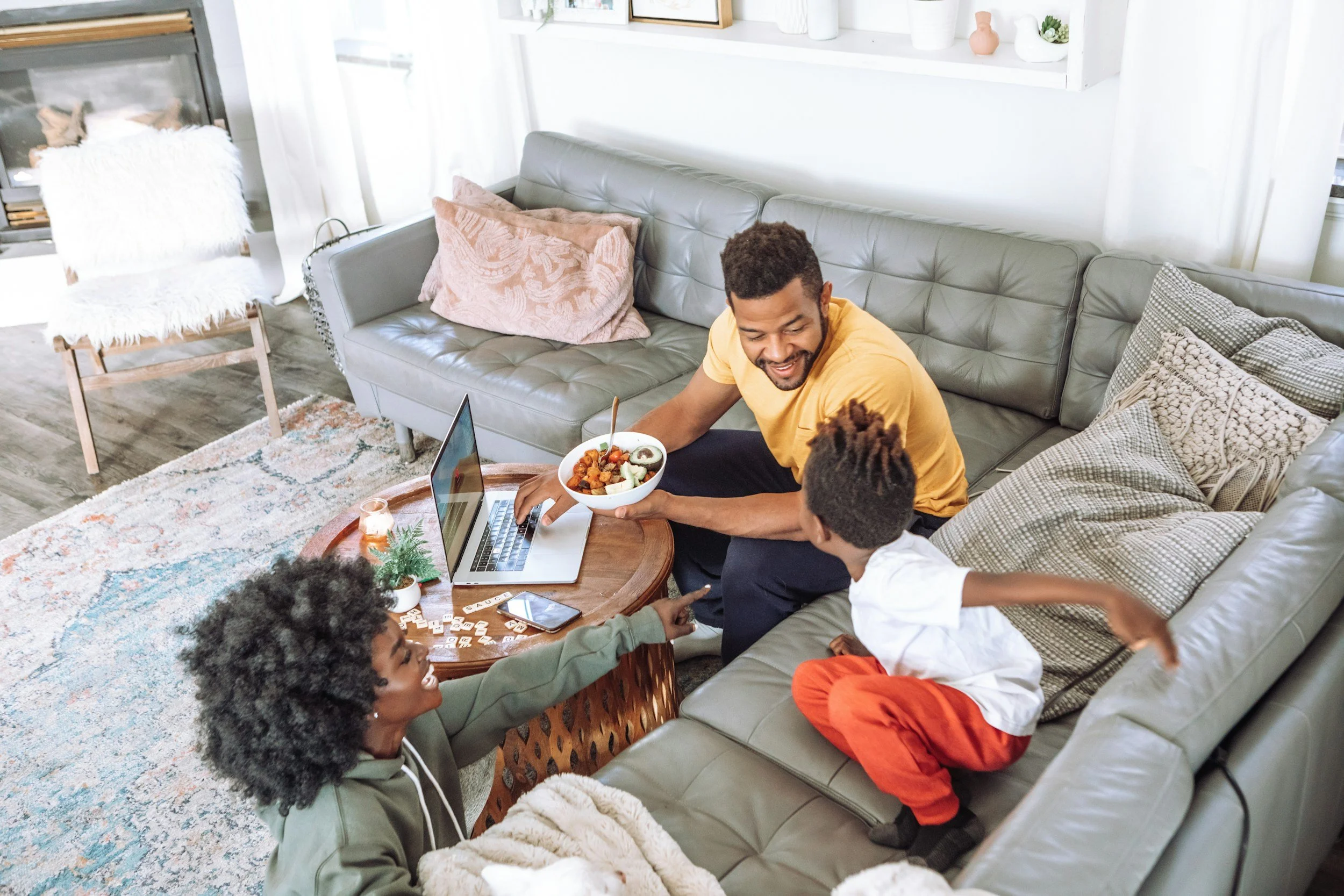 Two Black parents and a Black child laugh on a couch together. Families can feel more connected and calm together with the help of a trained play therapist in St. Louis.