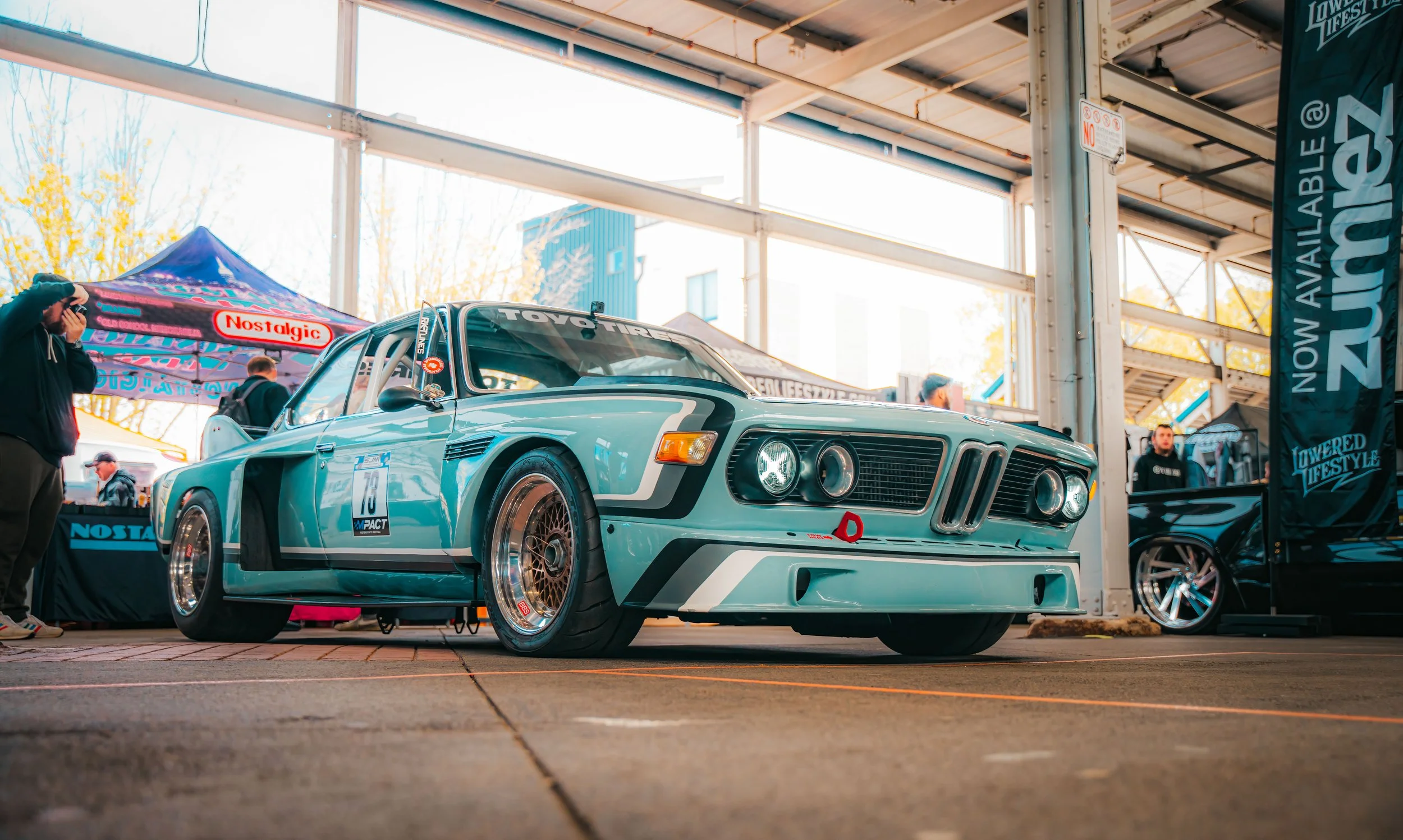A vintage racing car on display at an indoor car show with tents and other cars in the background.