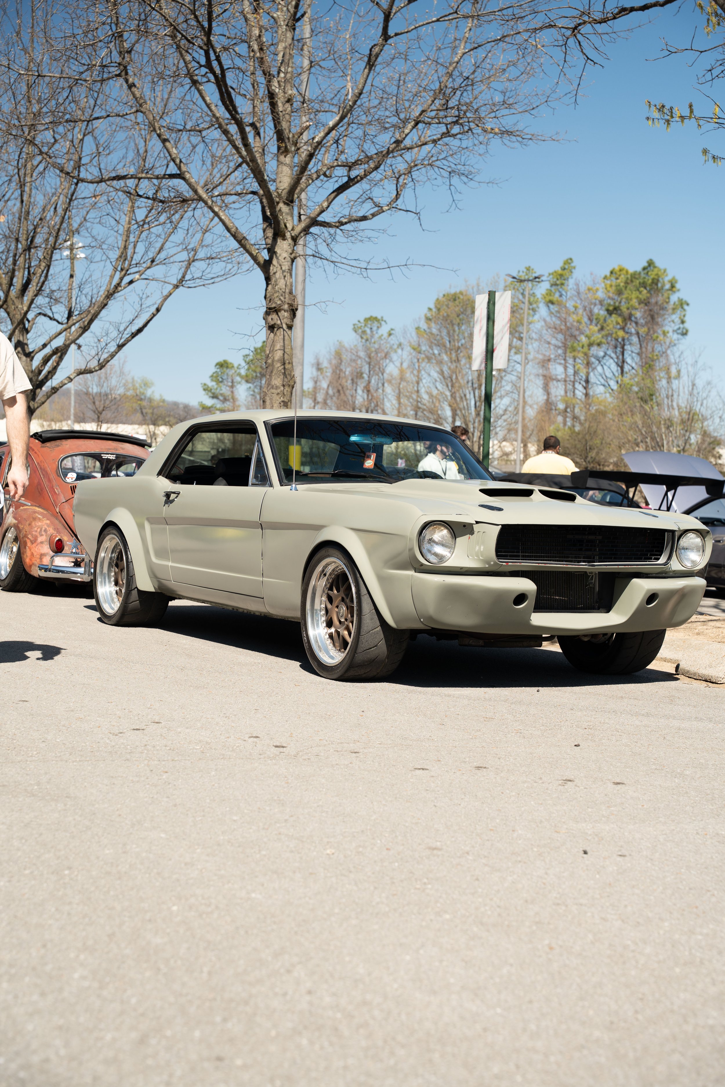 A vintage race car parked outdoors at a car show with a leafless tree and a clear blue sky in the background.