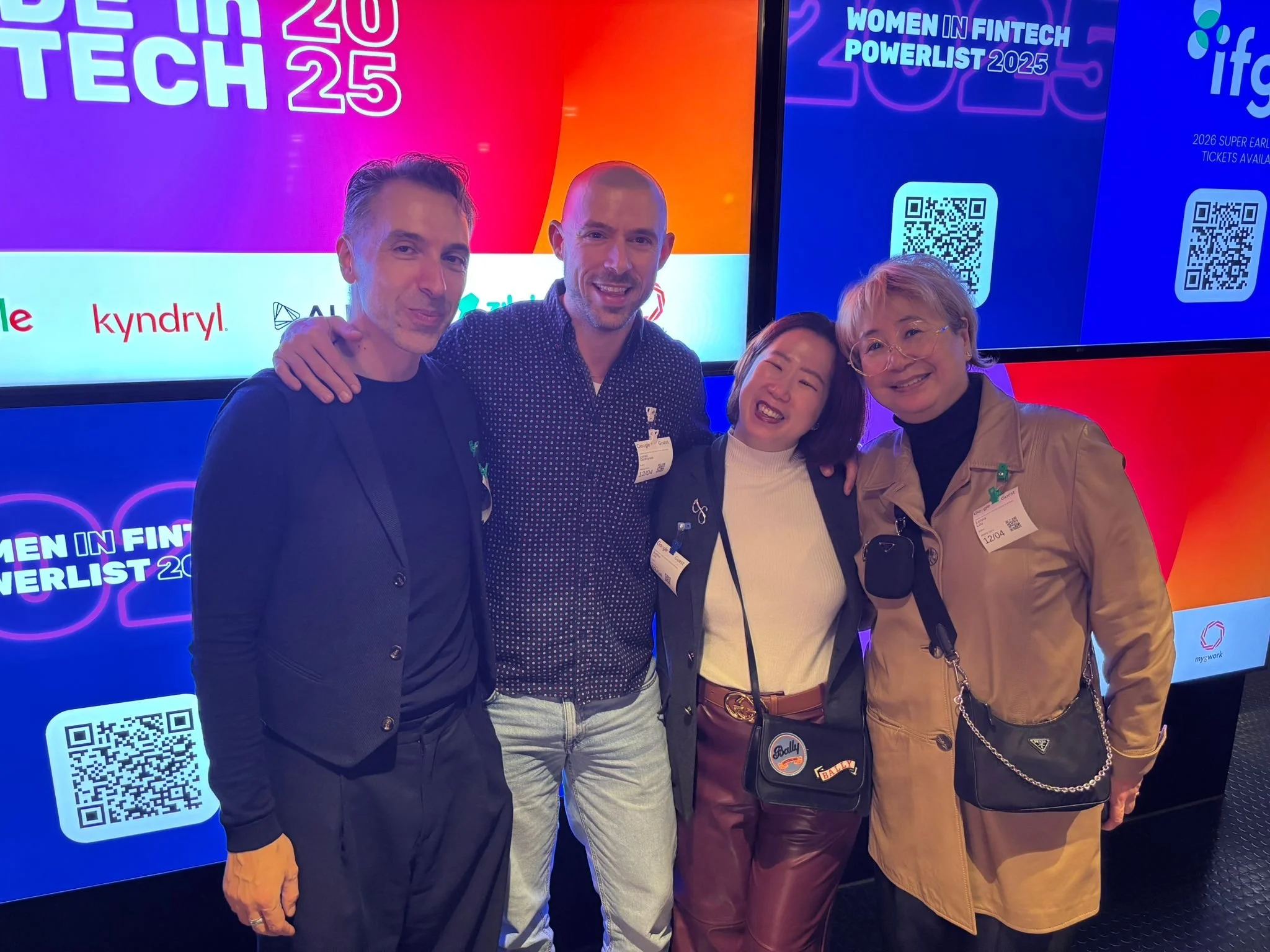 Four people smiling and standing together at the Women in Fintech Powerlist 2025 event, against a backdrop with colorful graphics and QR codes.