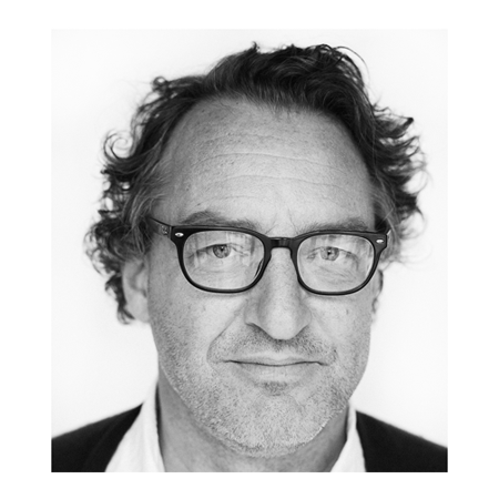 Close-up black and white photo of a middle-aged man with curly hair, glasses, and a slight smile.