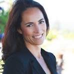 A woman with long dark hair smiling outdoors in natural light.