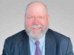 A confident public speaker who learned high-stakes presentation coaching for finance executives smiles against a gray background.
