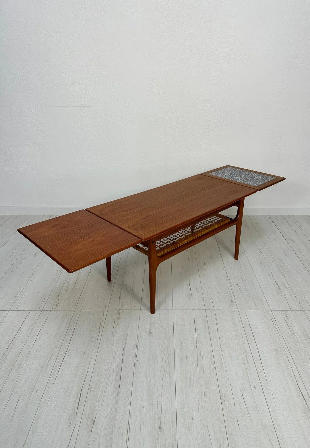 Extendable Teak Coffee Table by Trioh M&oslash;bler, 1960s

Two pull-out leaves take it from 105 to 183 cm, while a woven lower shelf adds storage and texture. Sculpted solid teak legs. Very good vintage condition; the woven shelf shows minor age-rel