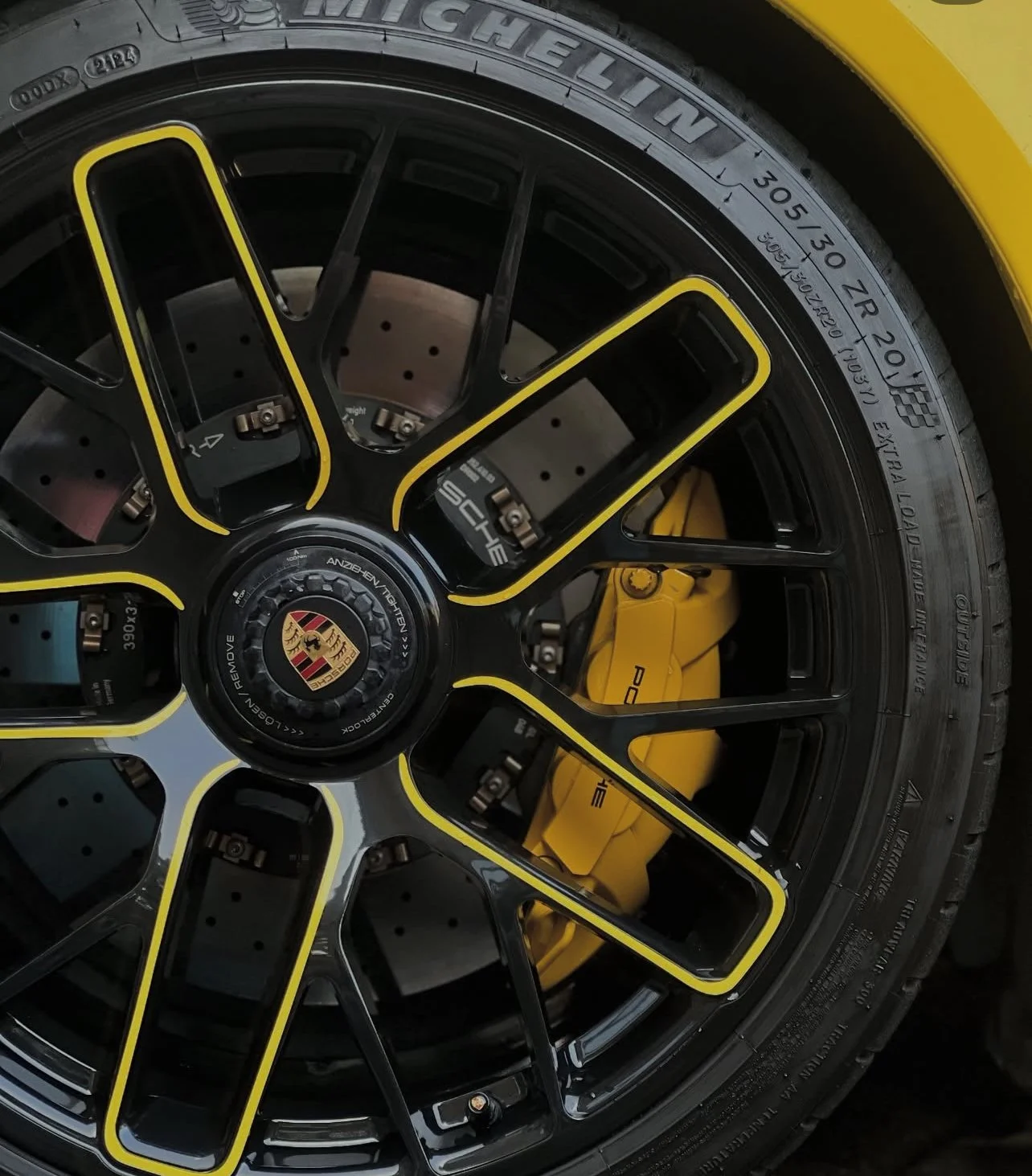 Close-up of a Porsche wheel with a black and yellow rim, yellow brake caliper, and Michelin tire.