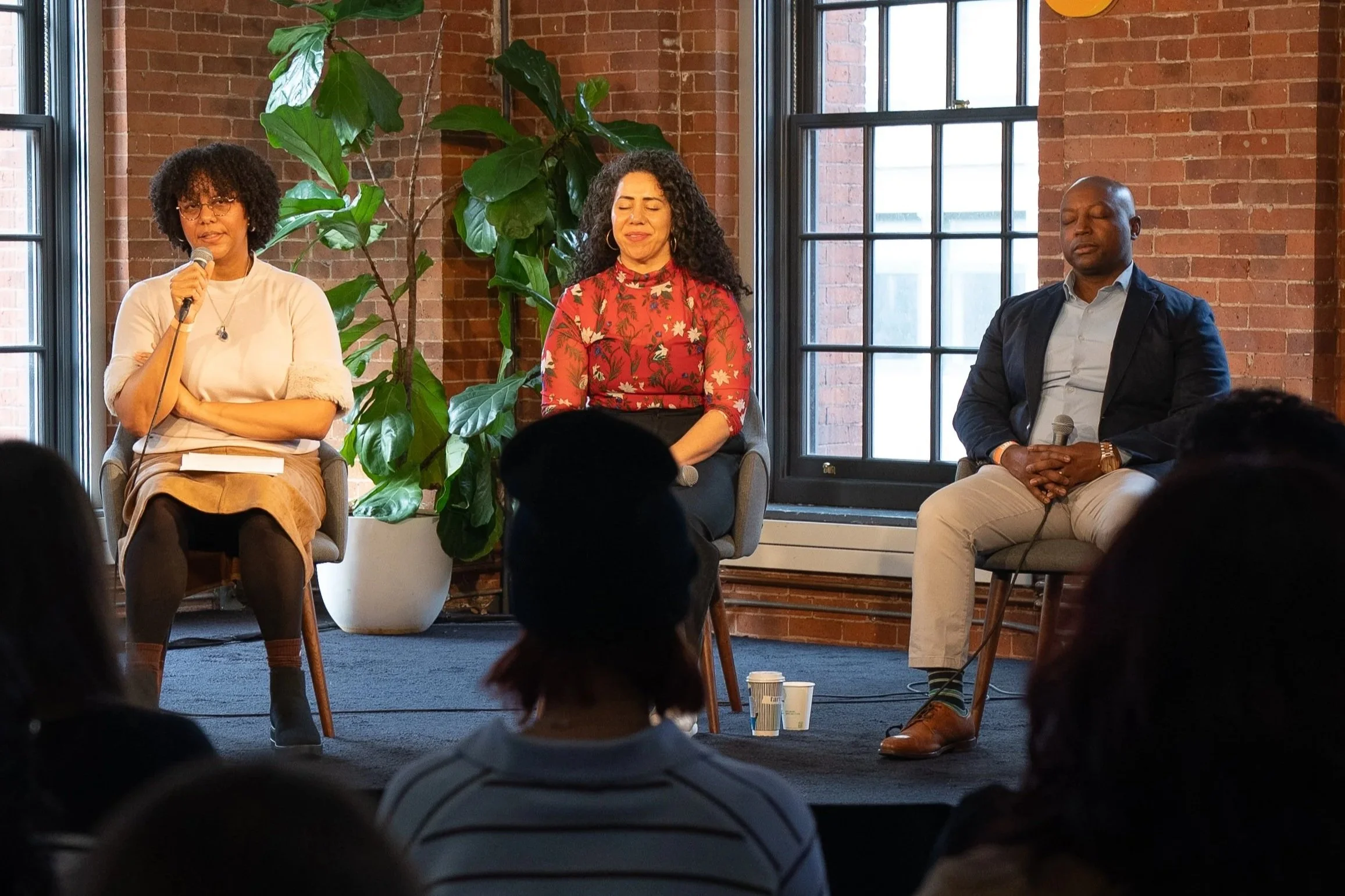 Group yoga event with diverse participants and panel discussion in a bright, plant-filled room.