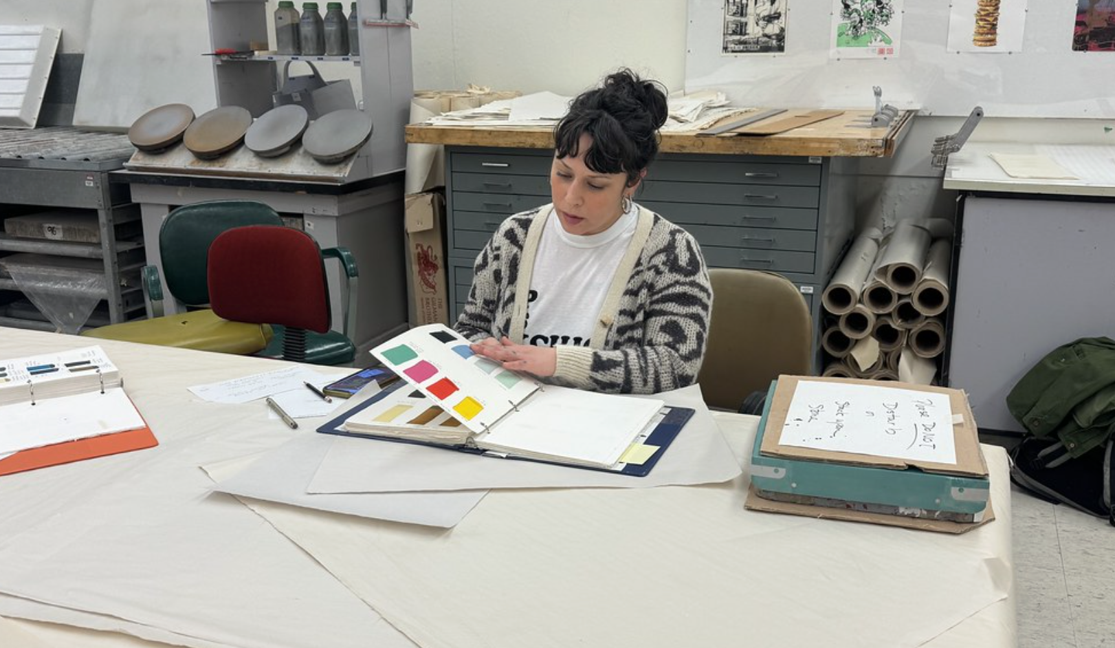 Julia flips through color swatches at a desk in a printshop at Illinois State University.
