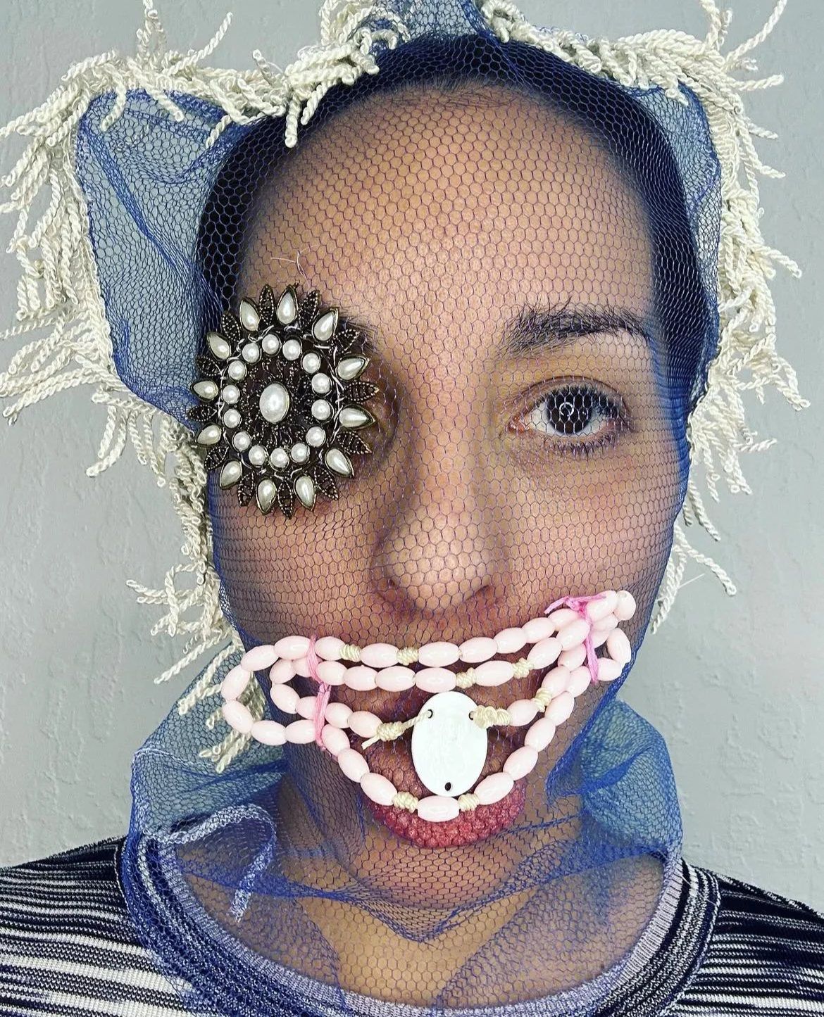 Blue net mask with pearl and pewter medallion eye, rosary bead mouth without cross, and white trim hair
