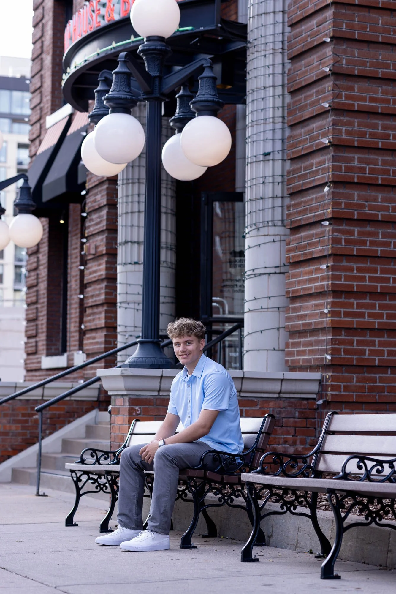 Senior portrait of a young man sitting on a bench in front of a brick building in Denver.