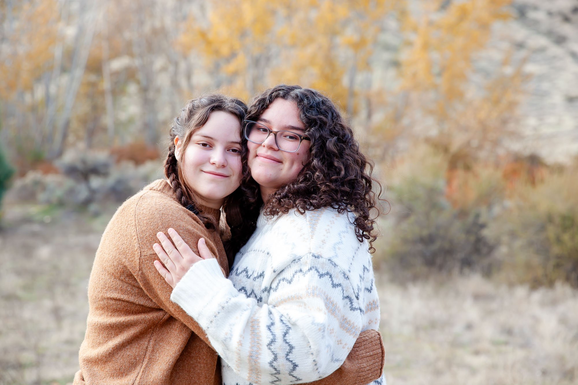 Two people hugging in an outdoor setting with autumn foliage in the background.