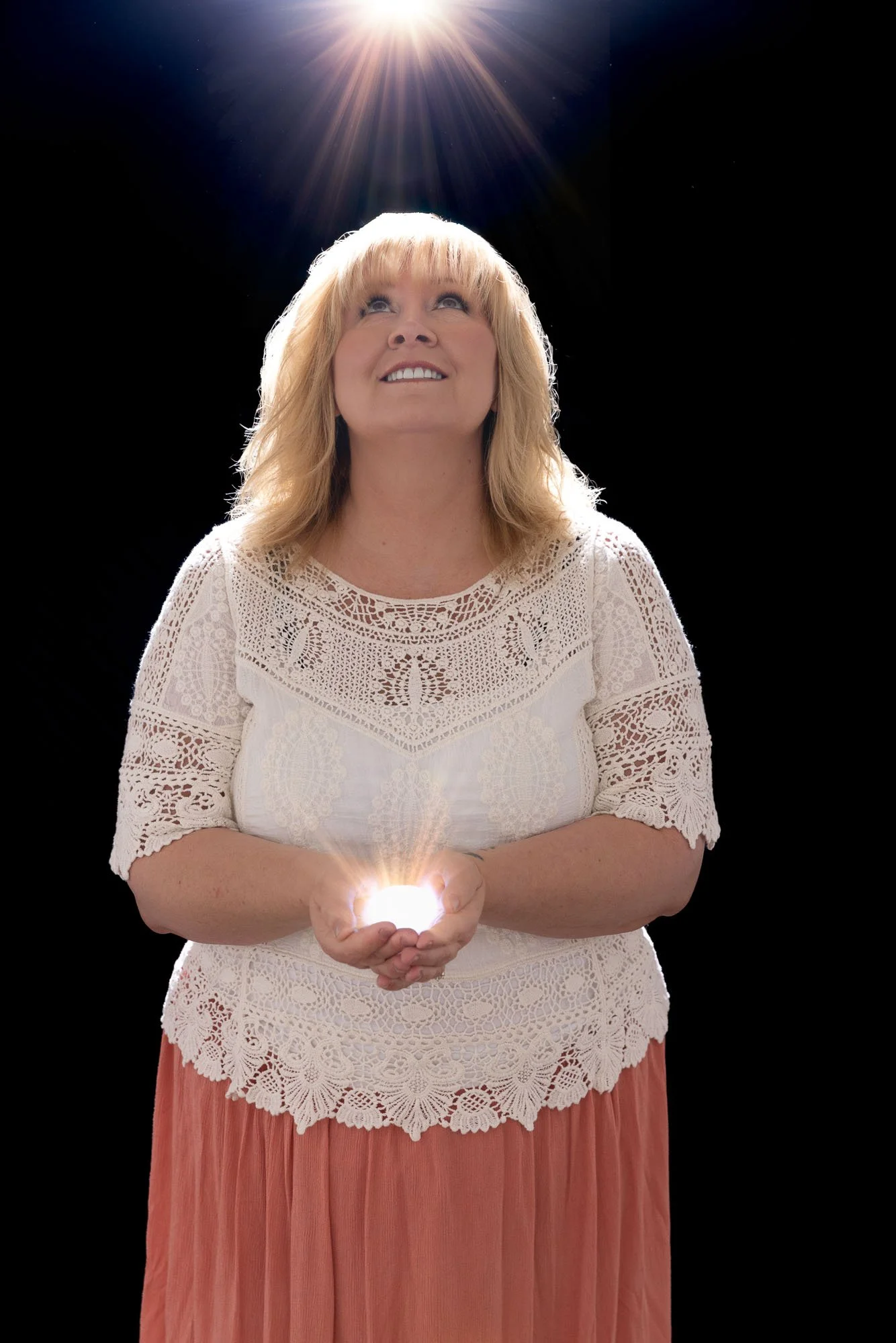 Image of a woman gazing upwards, with light shining down on her. She also has a light in her hands that is radiating out, representing the energy of reiki.