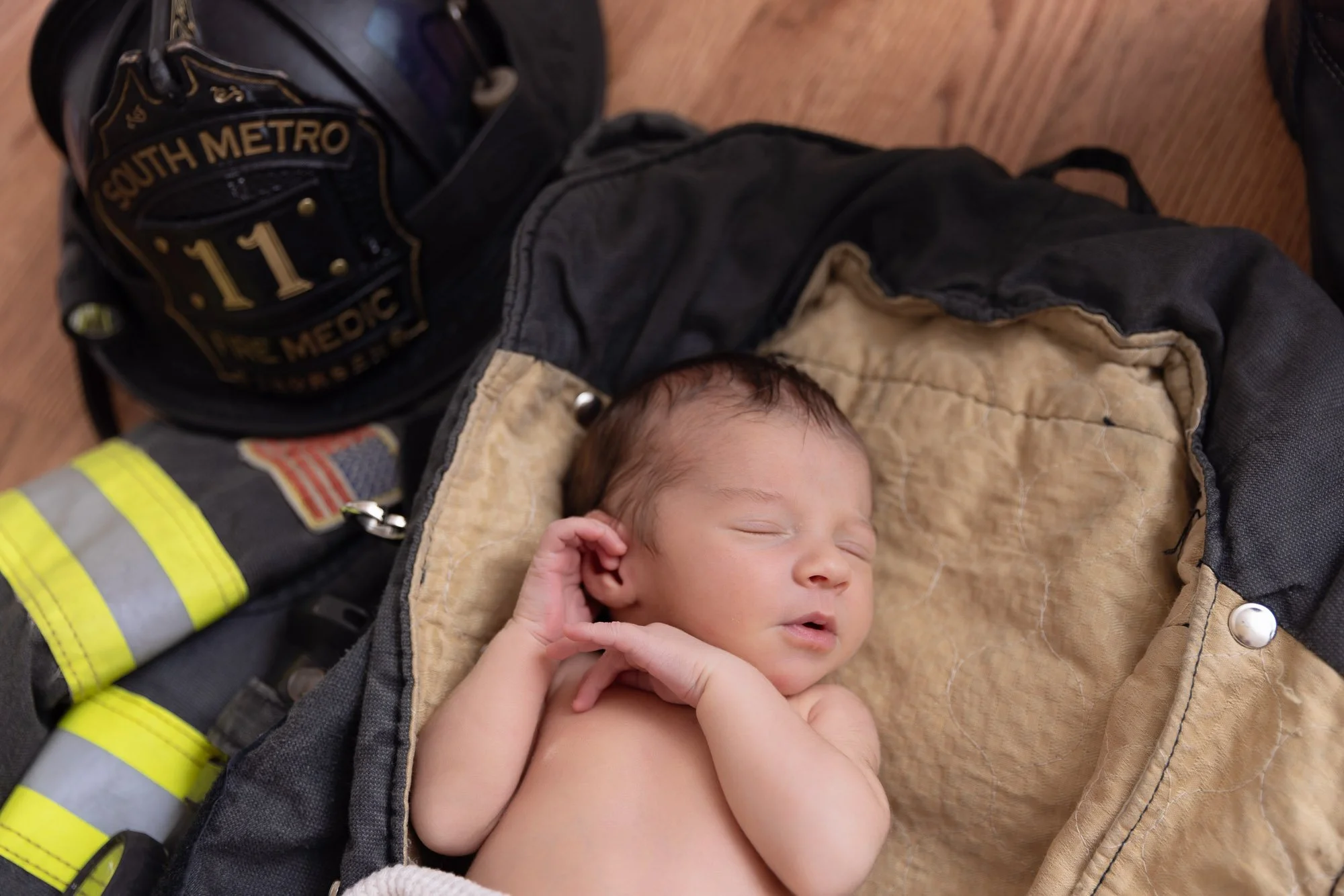 photo of a sleeping newborn baby laying in his father's firefighter jacket with a firefighter helmet to the side.