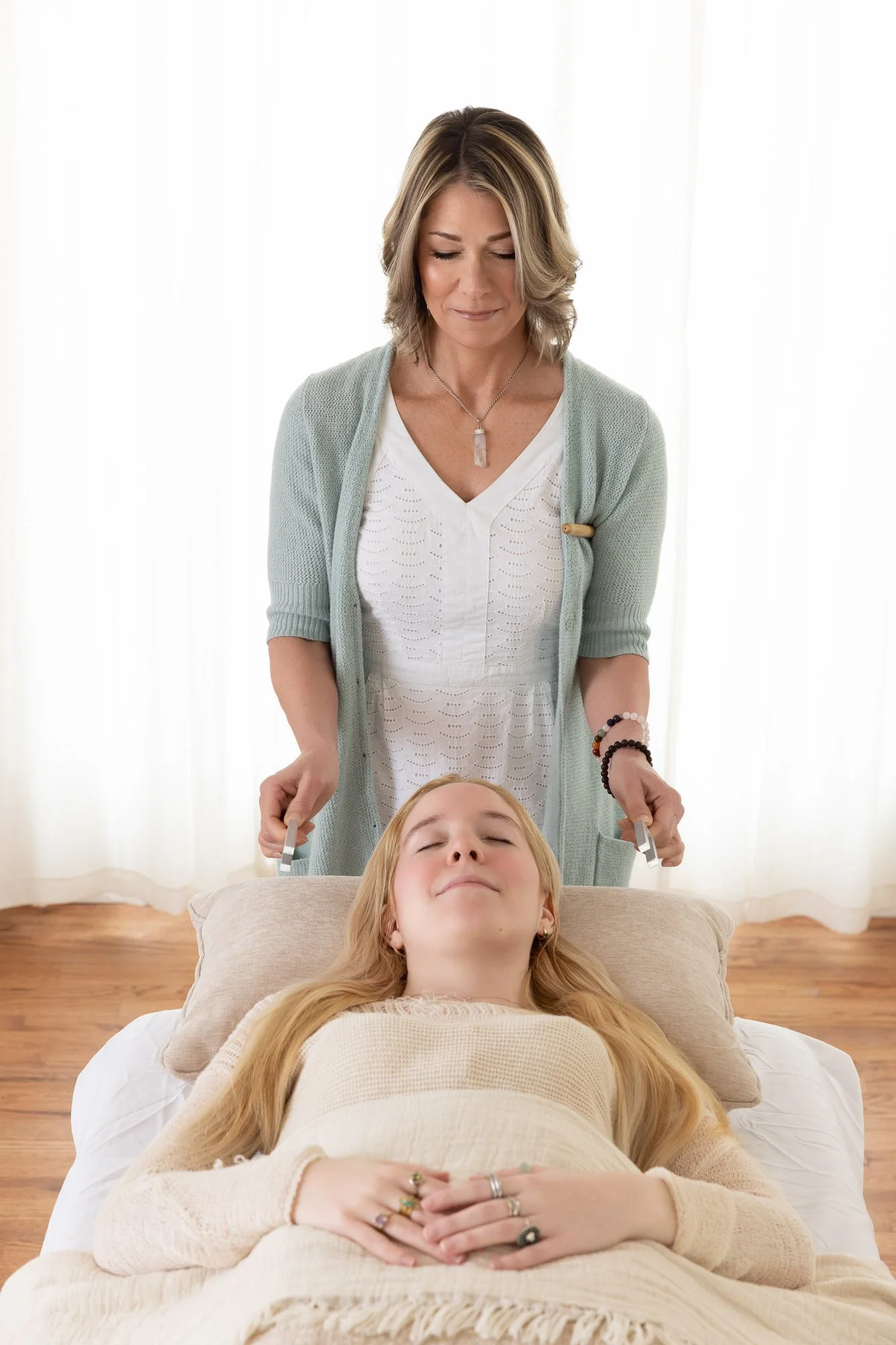 Portrait of a woman, a sound healer, holding tuning forks on both sides of her clients head. The photo is bright and backlit with a window.