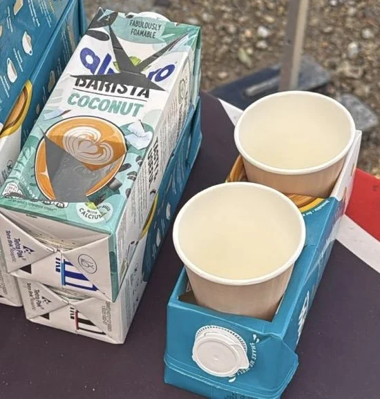 Two upcycled cartons of plant milk and two coffee cups placed inside a blue plant milk carton on a table.