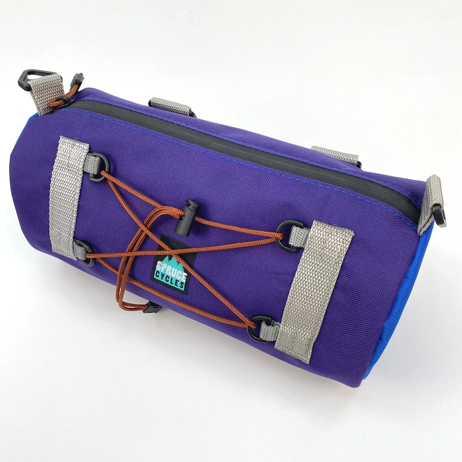 A purple bicycle handlebar bag with gray straps, a black zipper, and a blue and orange logo that says 'Spruce Cycles'. It features orange bungee cords on the outside.