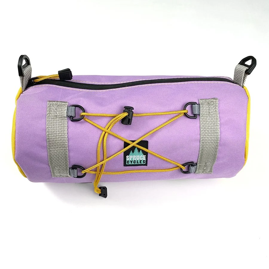 A purple bicycle handlebar bag with yellow and gray accents, featuring multiple straps and a logo that says "Spruce Cycles."