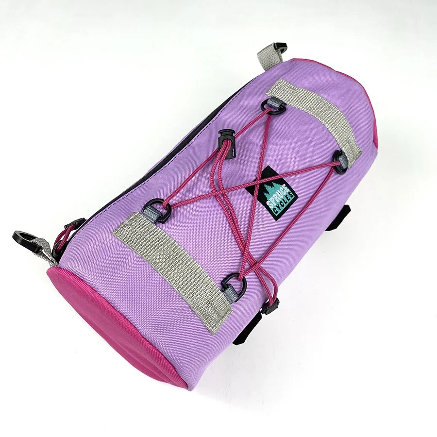 A purple and pink sports duffel bag with a black logo that reads 'Sports Cycles' on the side, featuring pink bungee cords on the top for securing items.
