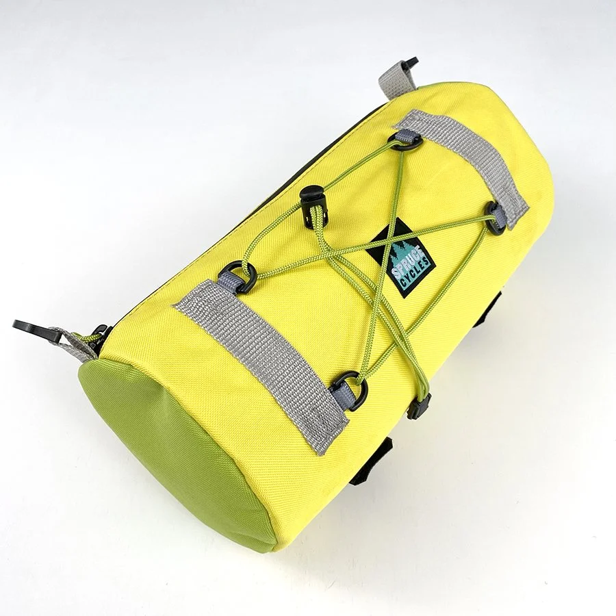 Yellow bike saddlebag with gray straps and green bungee cords attached for securing it to a bike, with a small logo that reads 'Super Cycles'.