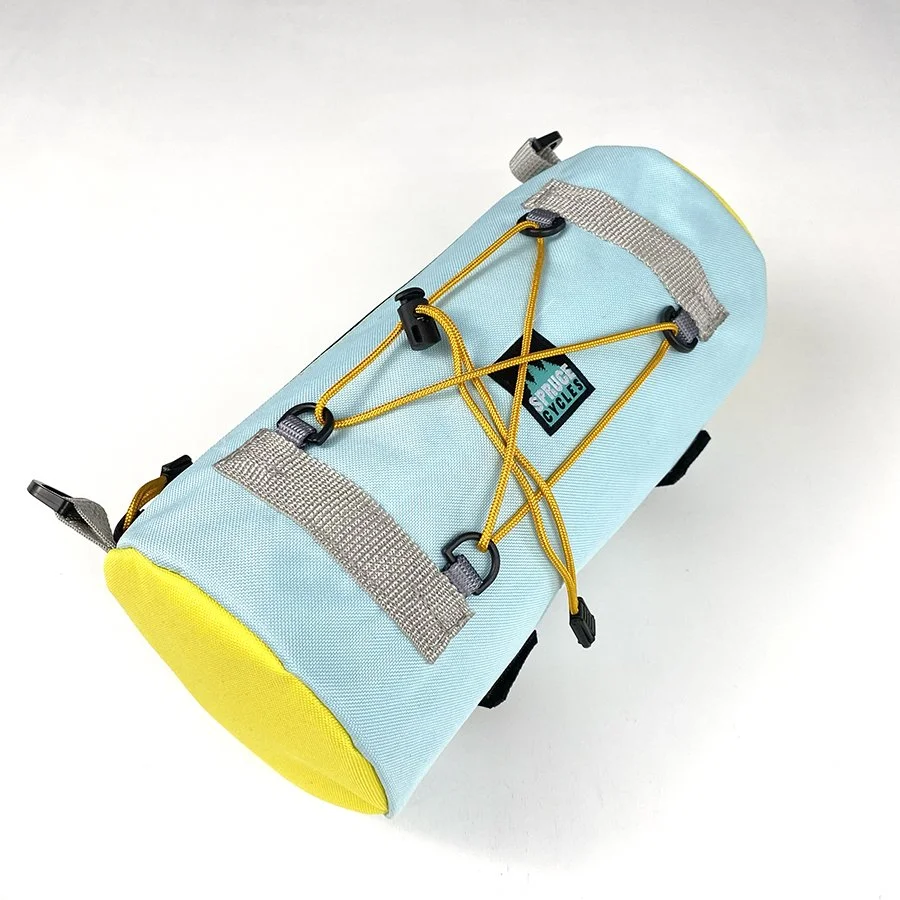 Light blue and yellow bicycle saddlebag with gray straps and yellow bungee cords for securing items, mounted on a white background.