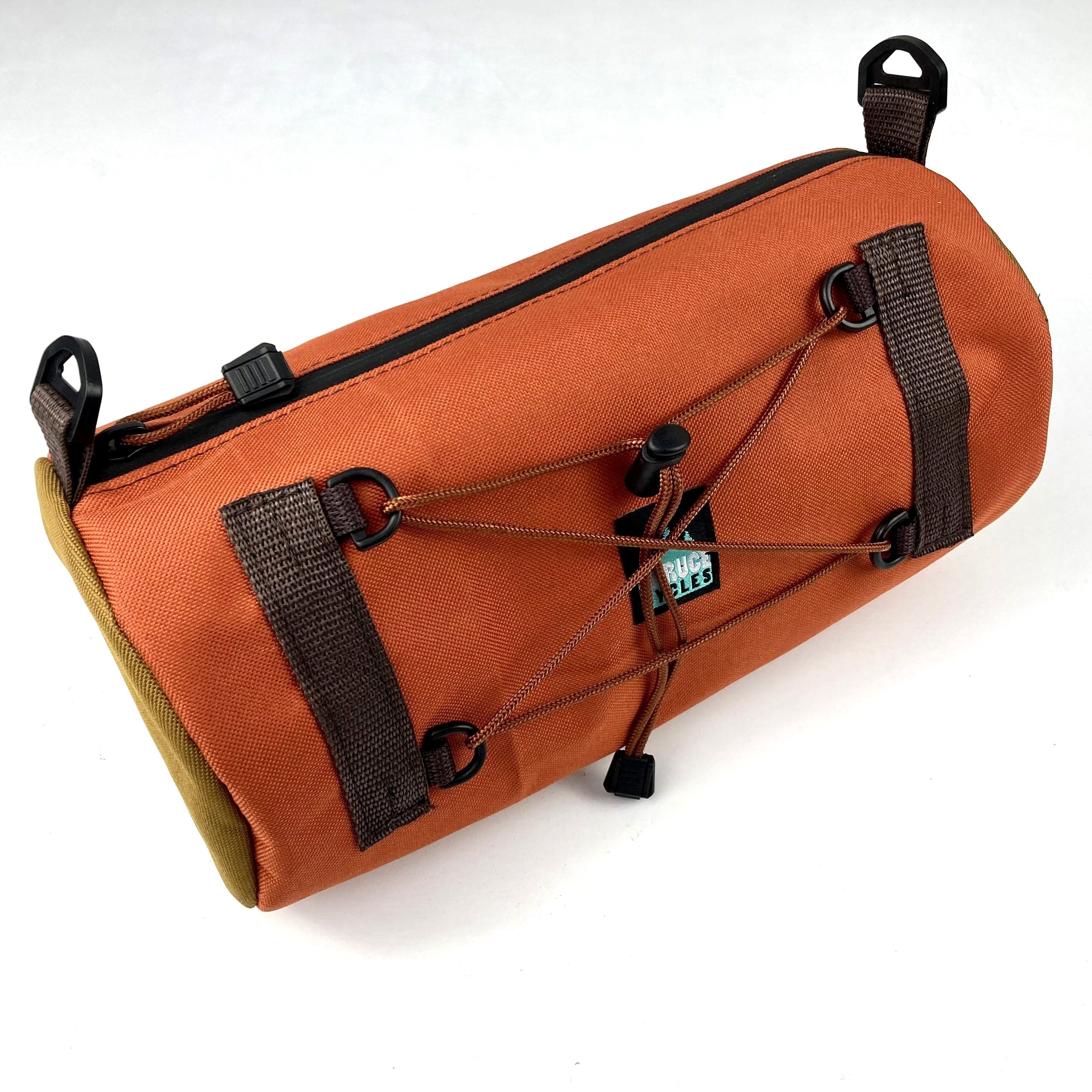 Orange and olive green bicycle saddle bag with black zippered closure, brown straps with hooks, and a bungee cord with black plastic end caps secured inside. Signature logo tag visible on the front.