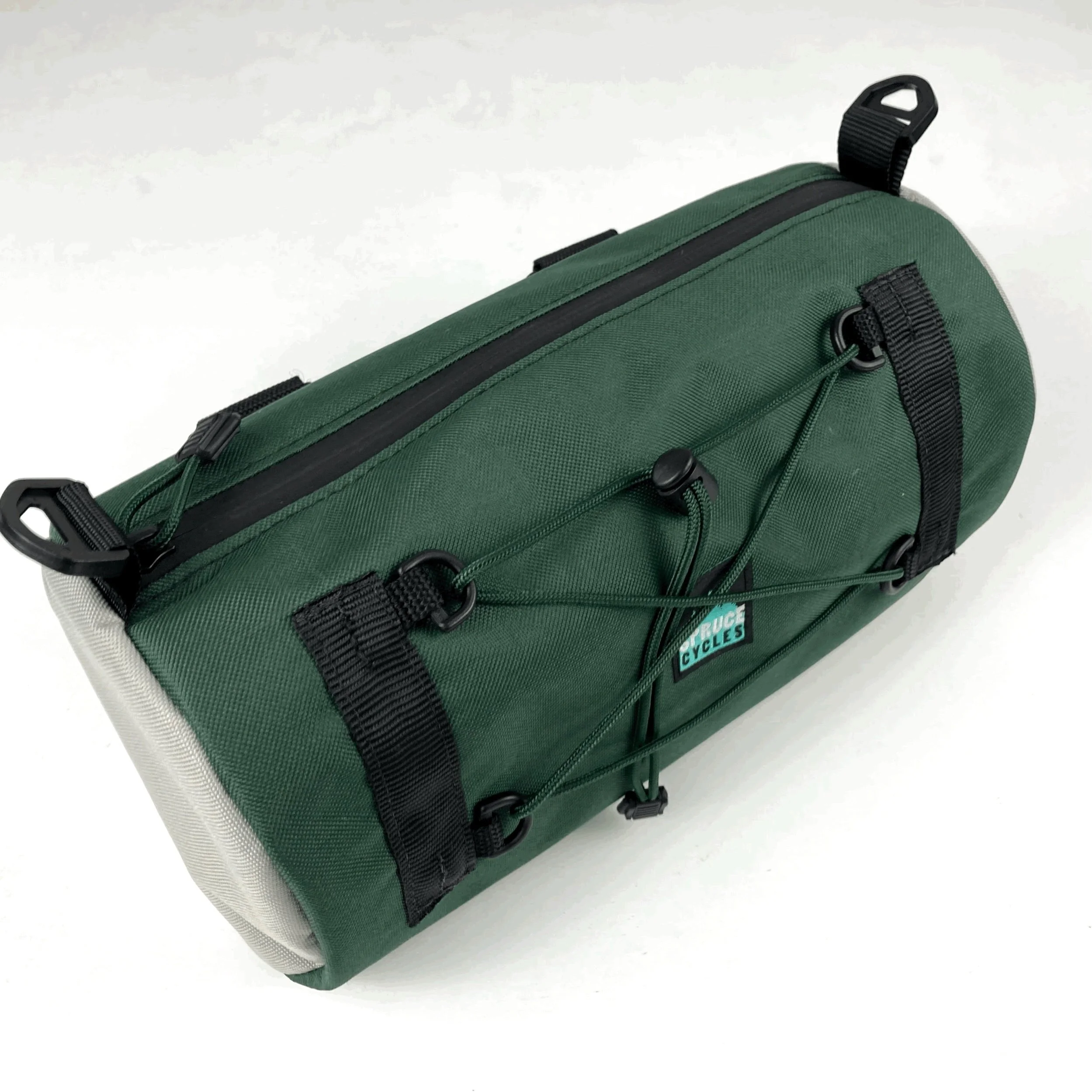A green bicycle saddle bag with black straps, zippers, and bungee cords, placed on a white surface.