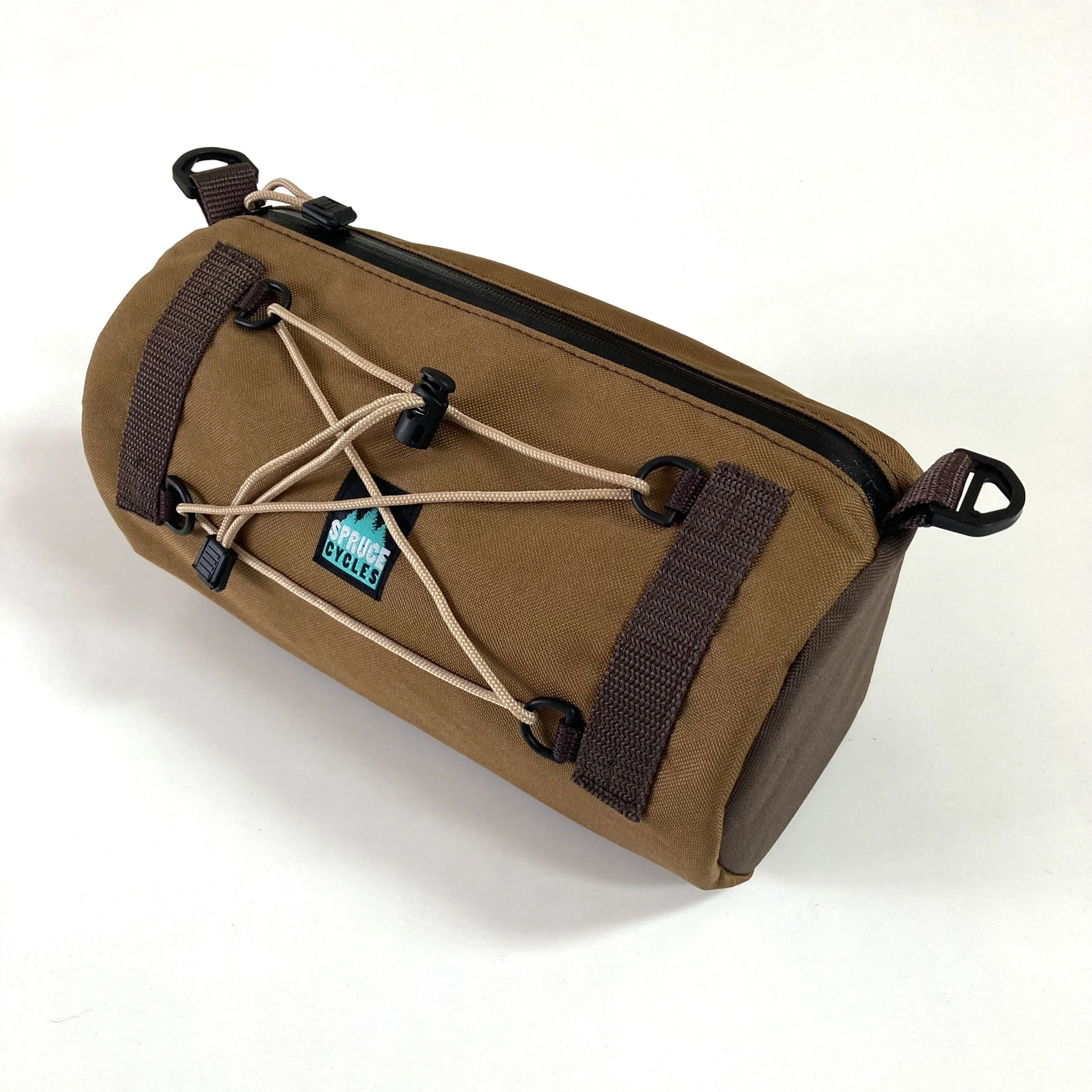 Brown outdoor gear bag with black zipper, elastic cord with locks, and a small branded patch reading "Spruce Cycles" on a white background.