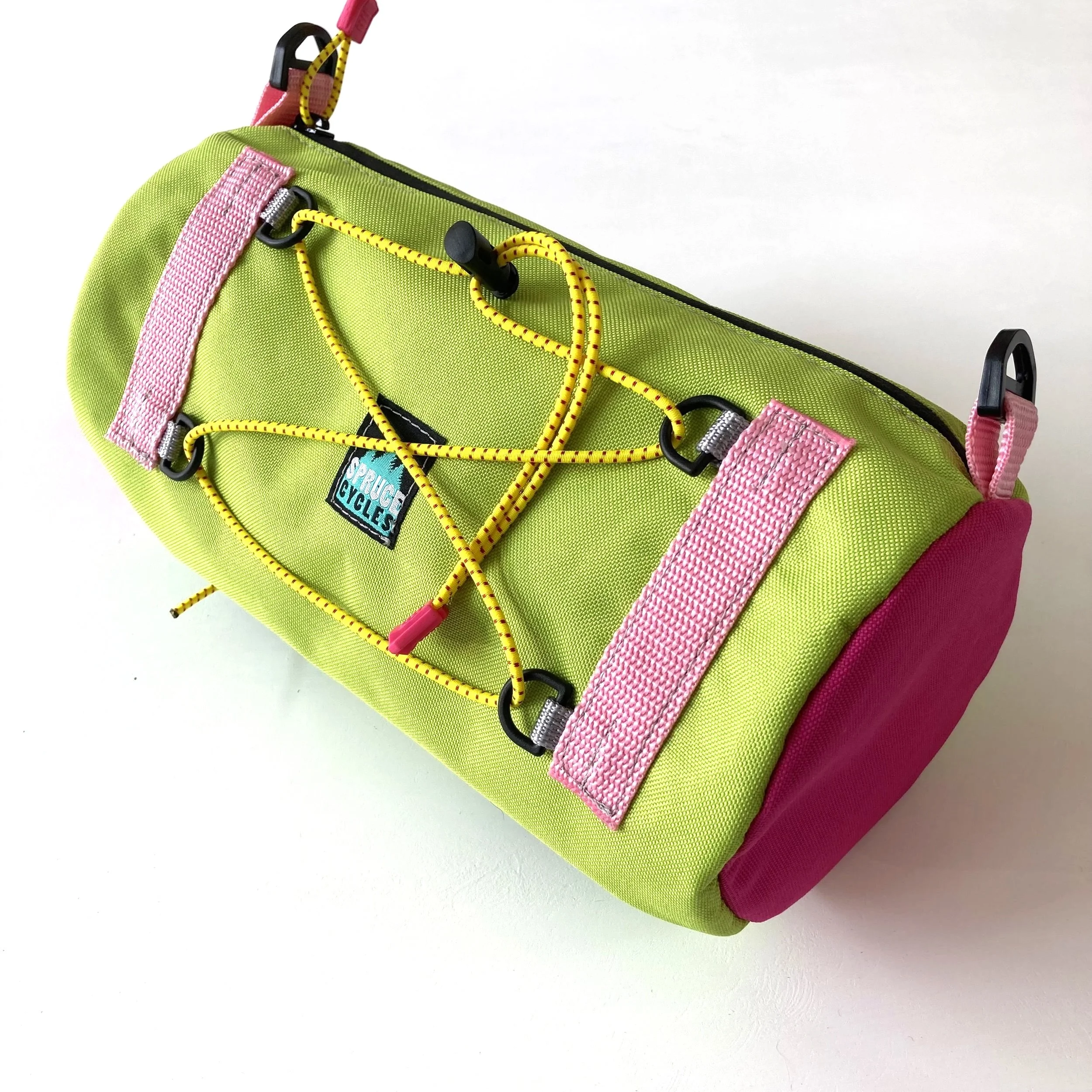 Green and pink fabric lunch bag with yellow bungee cord on top.