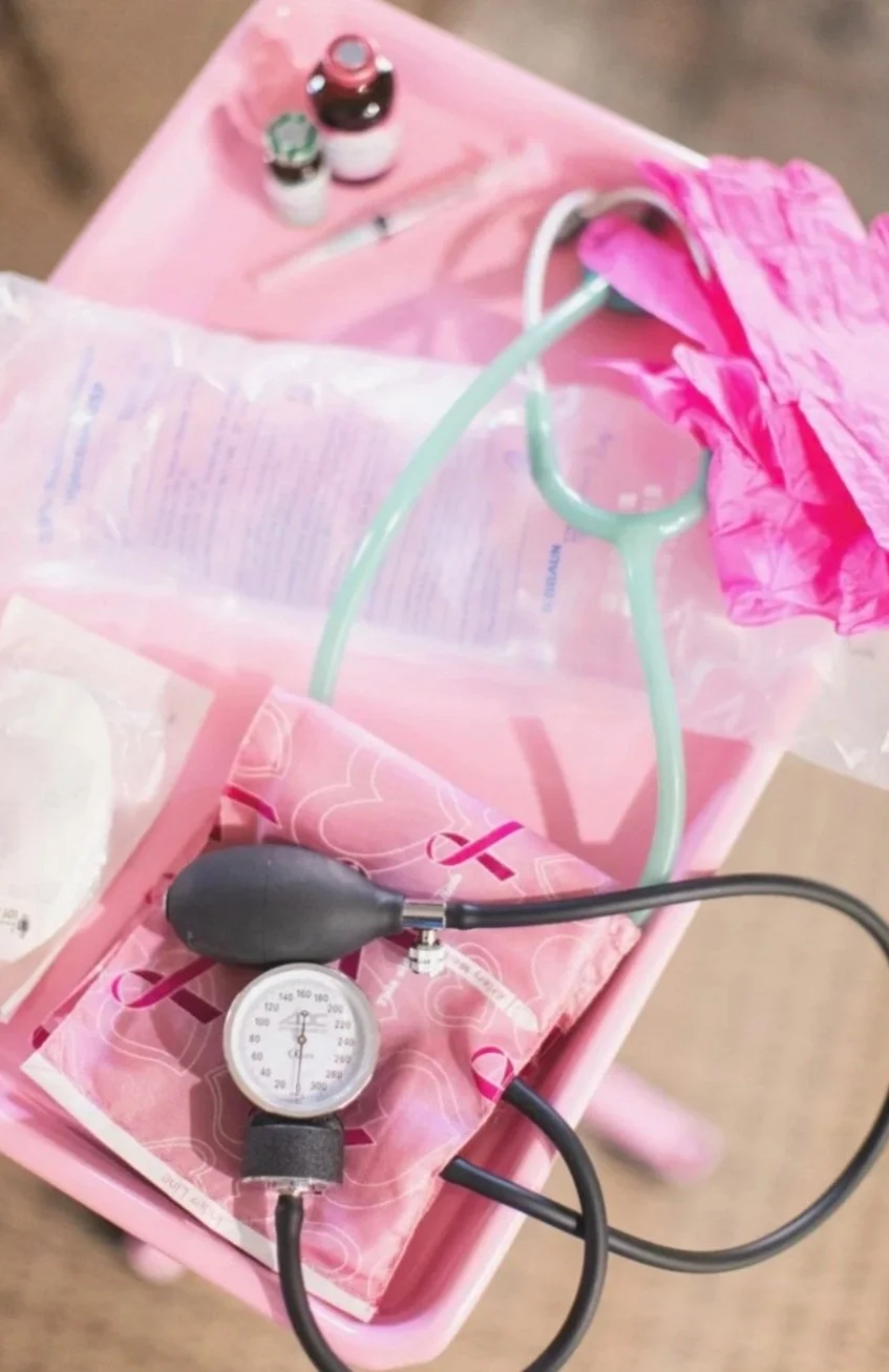 A pink healthcare tray with a blood pressure cuff, a stethoscope, and medication bottles.