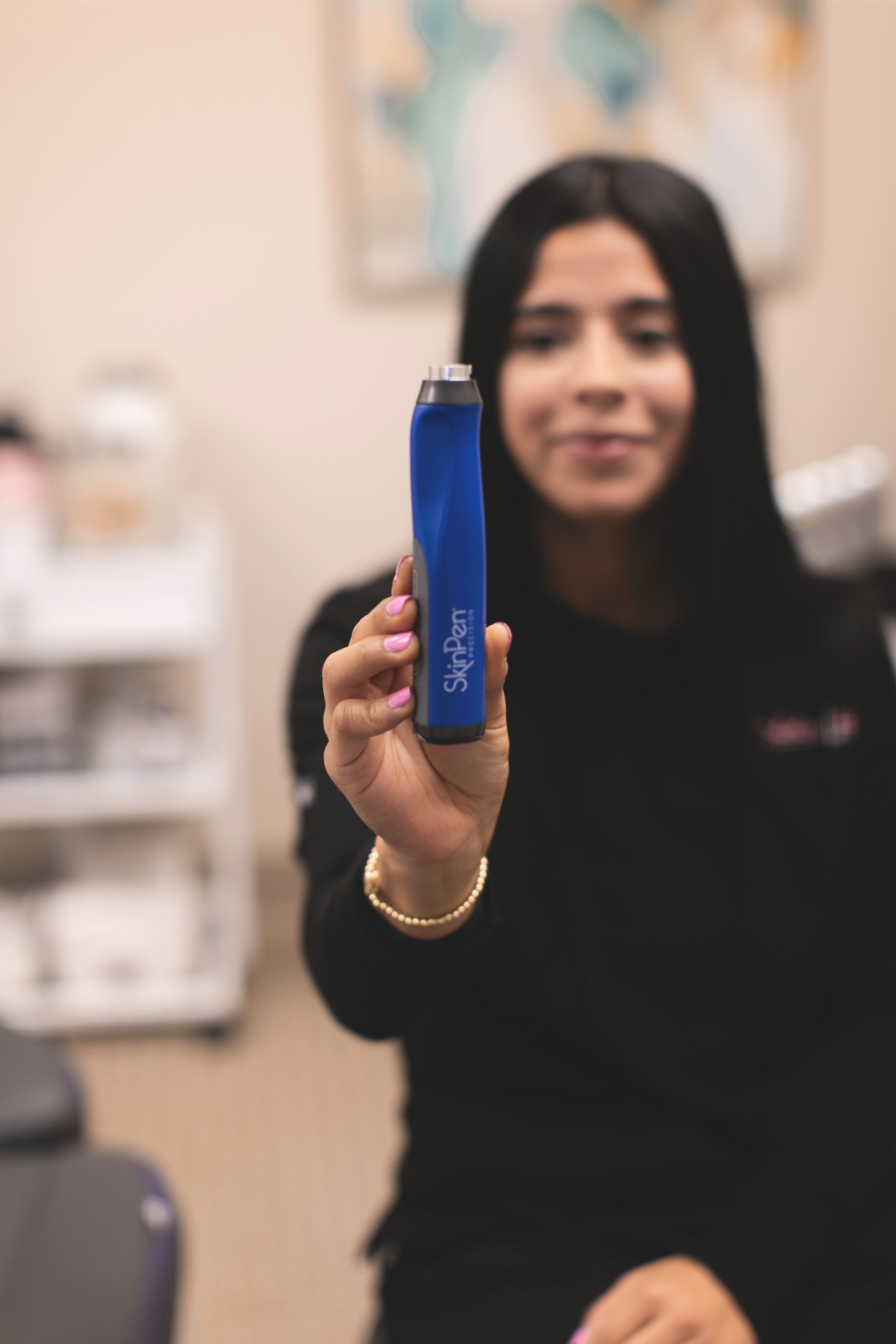 A woman holding a blue SkinPen device towards the camera, with a blurred background.