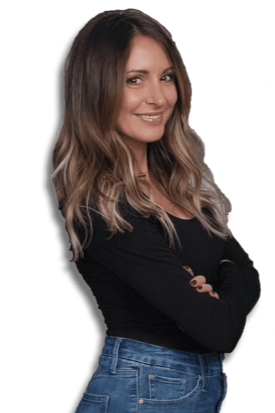 A woman with long, wavy brown hair smiling with her arms crossed, wearing a black top and blue jeans.