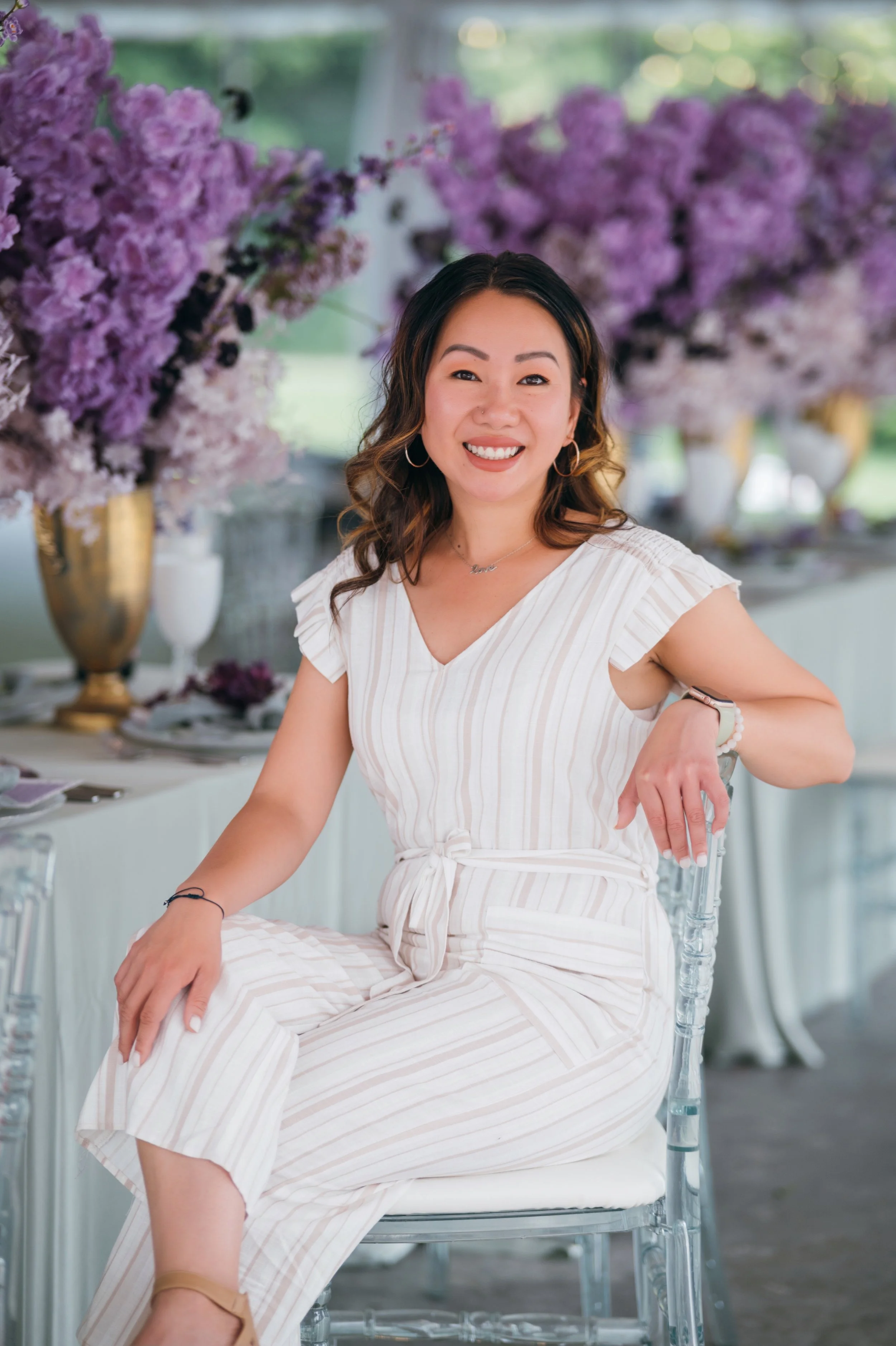 Kim was seated at an elegant event, wearing a striped dress, surrounded by lavish lavender floral arrangements and table settings.
