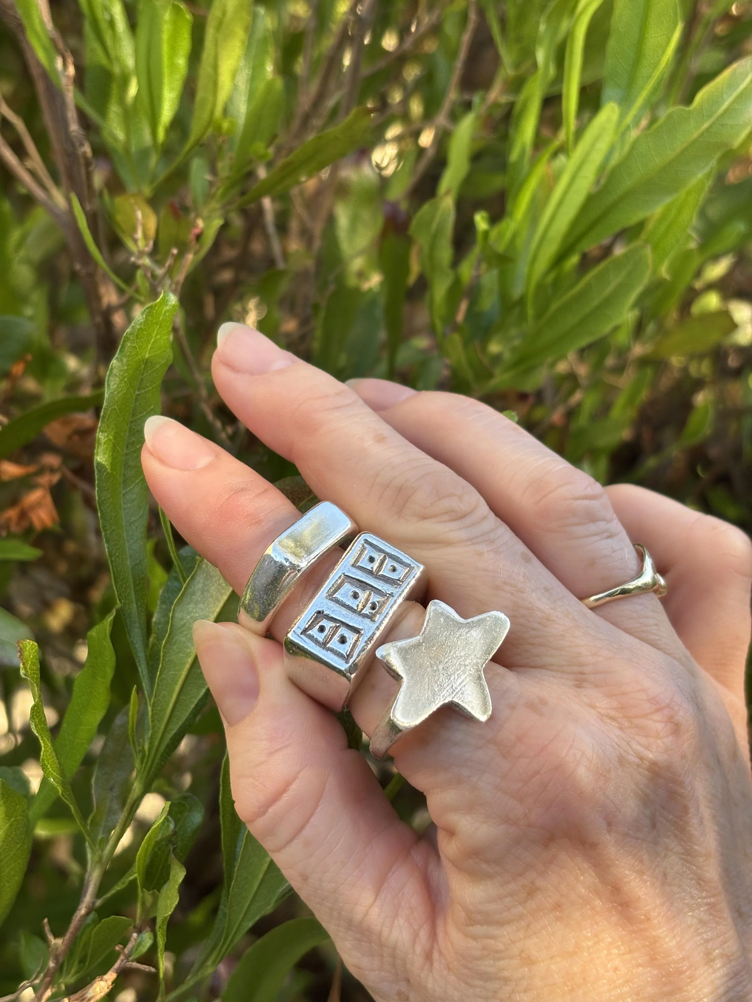 woman's hand with three silver rings on her index finger in front of plants
