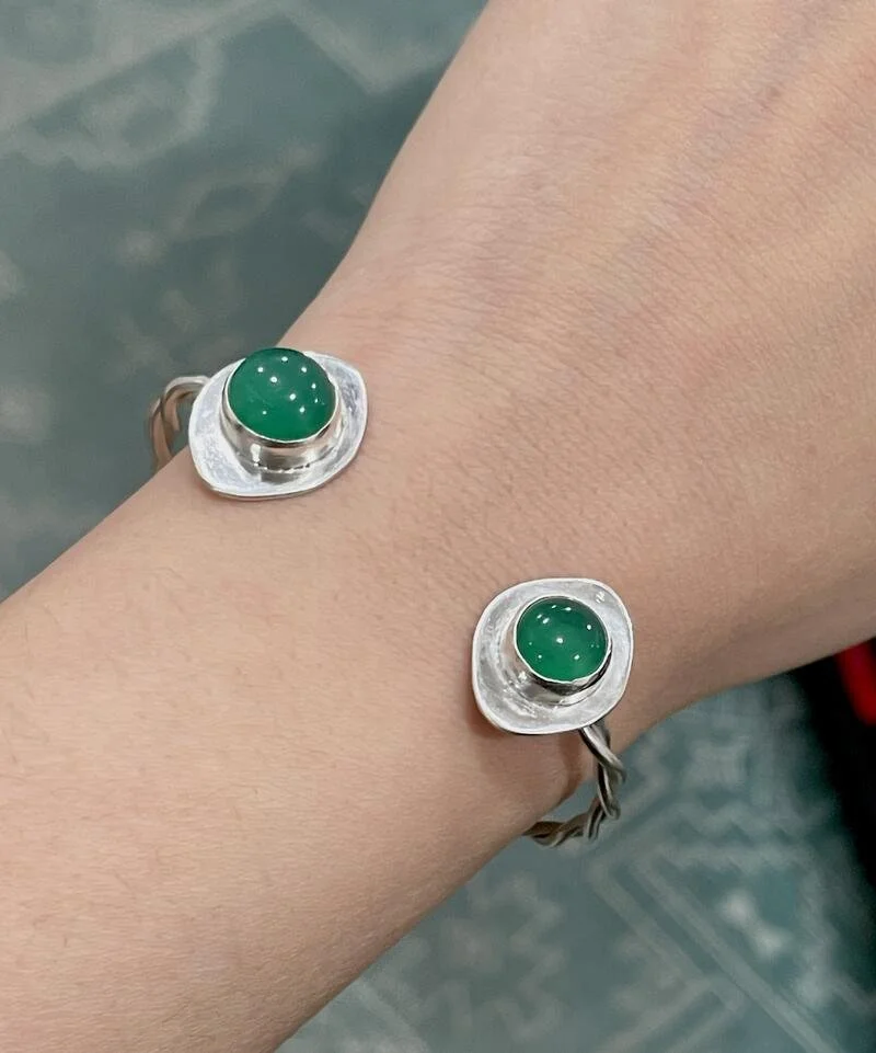 A person's wrist wearing a bracelet with green oval stones at each end.