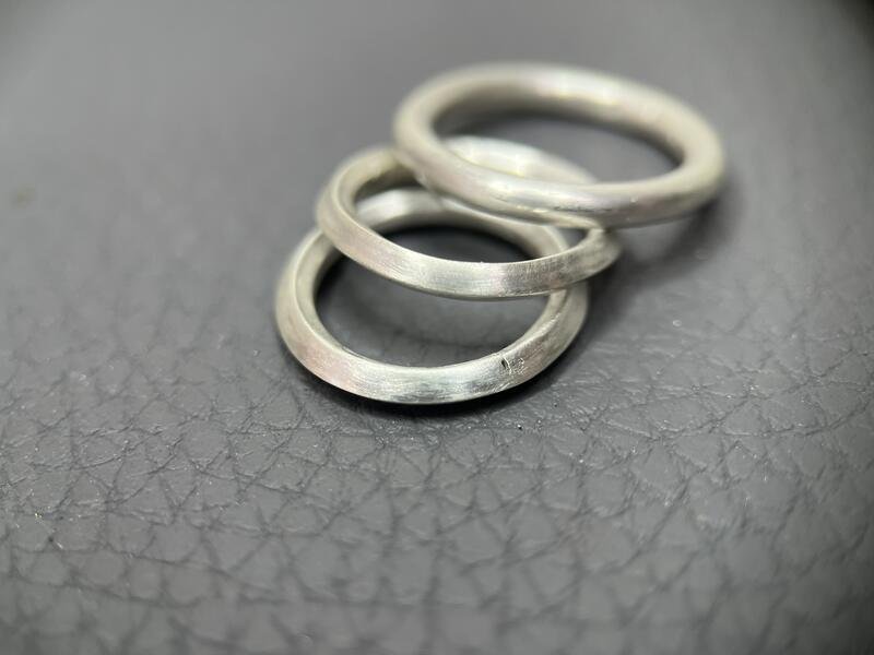 Three silver rings fanned out atop each other on a textured grey surface.