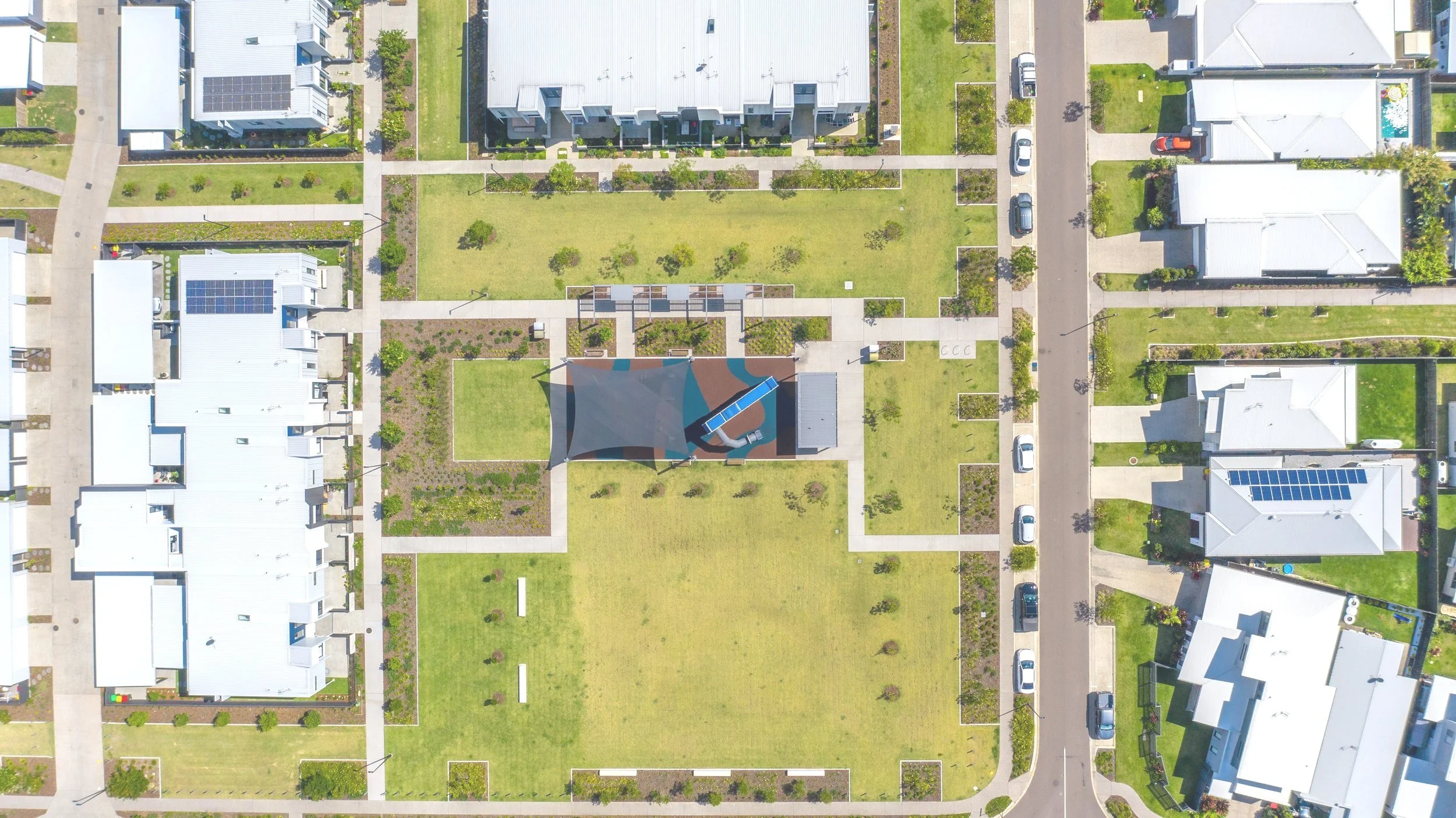 Aerial view of a residential neighborhood with houses, green lawns, walkways, and a central playground with shade structure and slides.