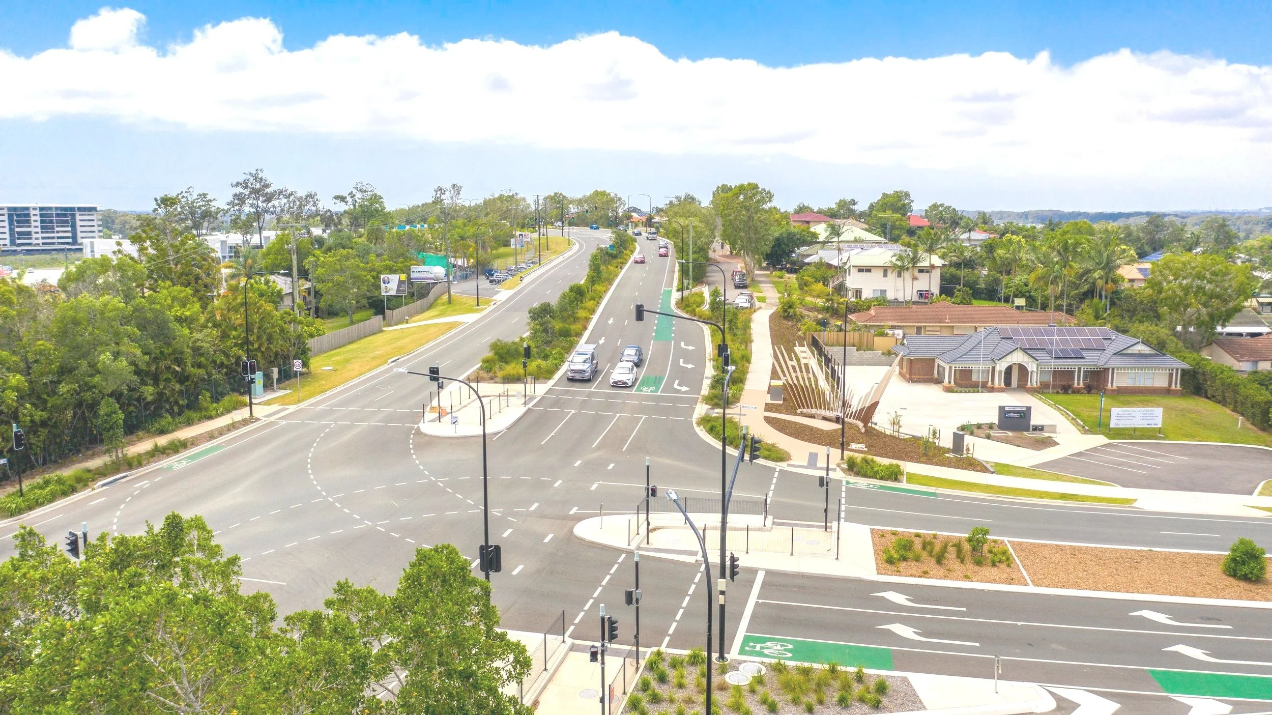An aerial view of a suburban intersection with traffic lights, cars, bike lanes, crosswalks, and surrounding residential houses and trees.