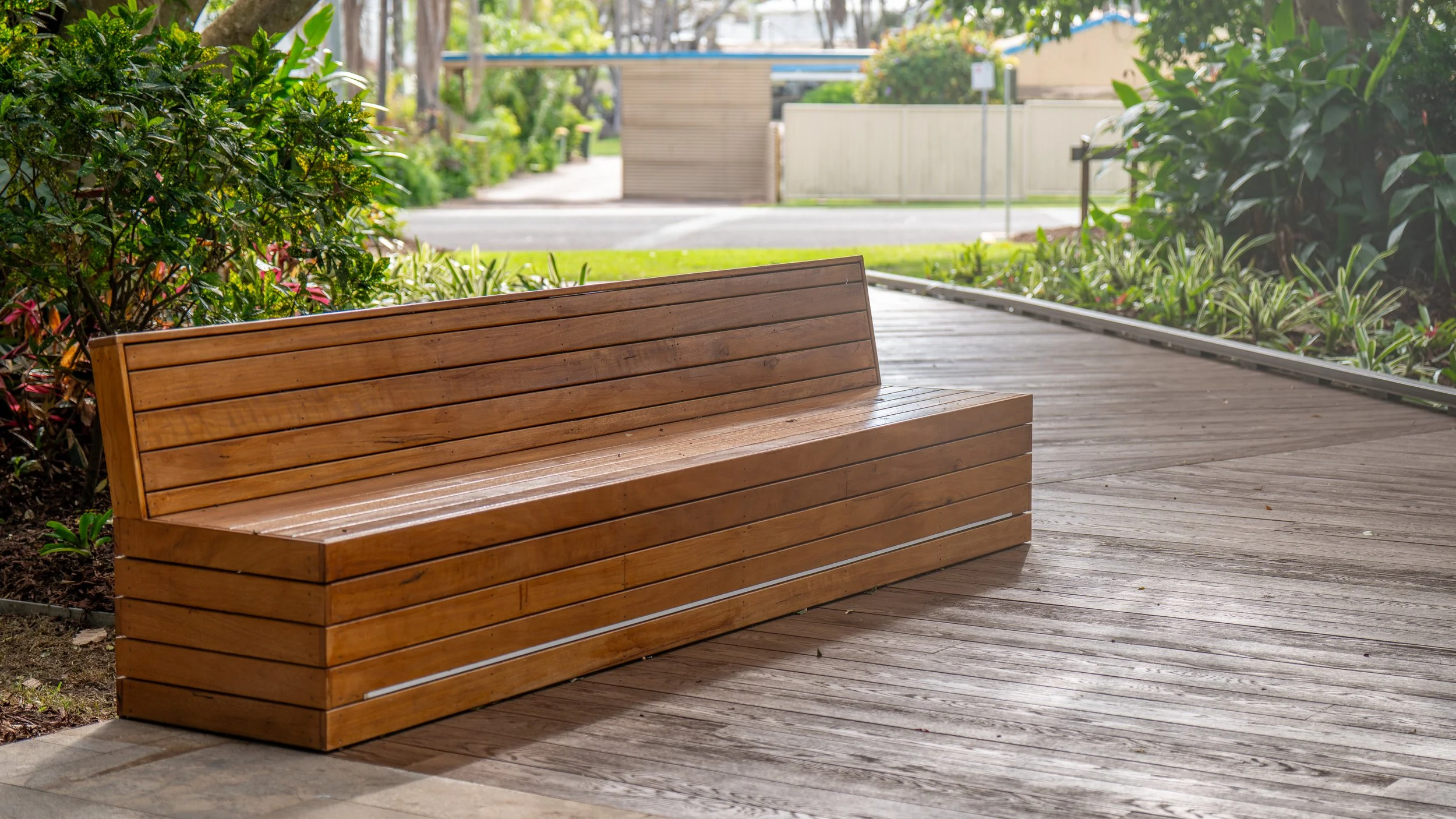 A wooden park bench on a wooden walkway surrounded by greenery in an outdoor park setting.
