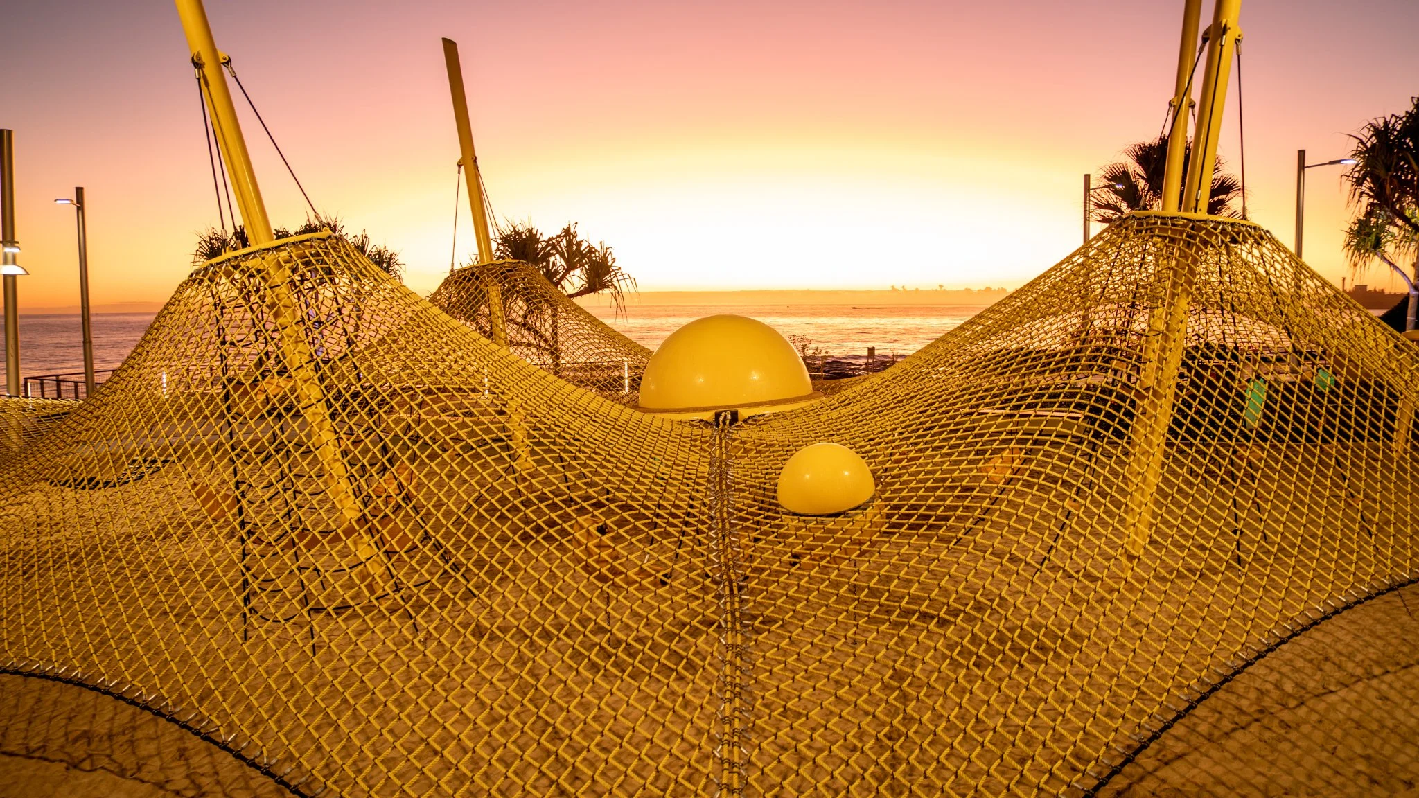 Yellow netting and dome structures with a sunset view of the ocean and palm trees in the background.